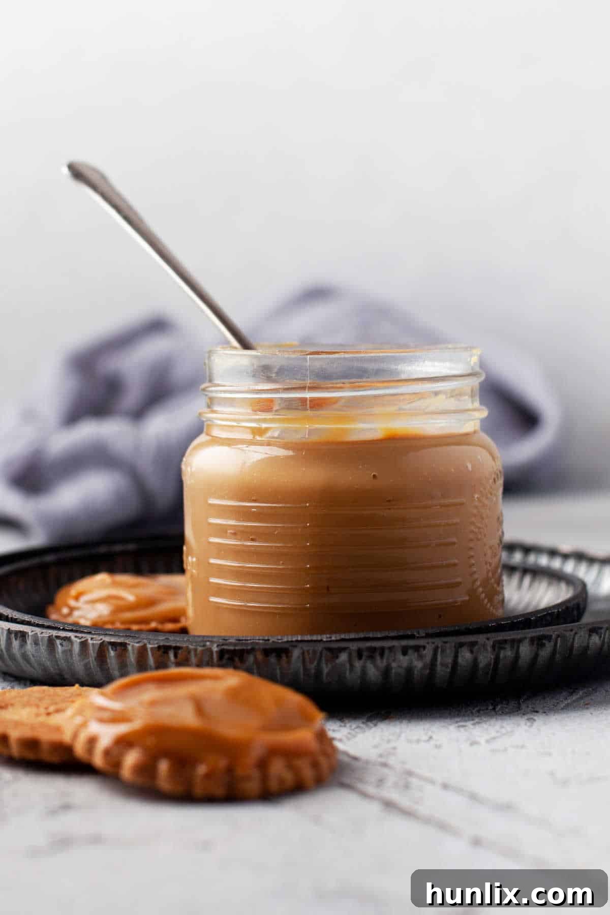 A glass jar of homemade dulce de leche, perfectly golden and creamy, with a spoon ready for tasting.