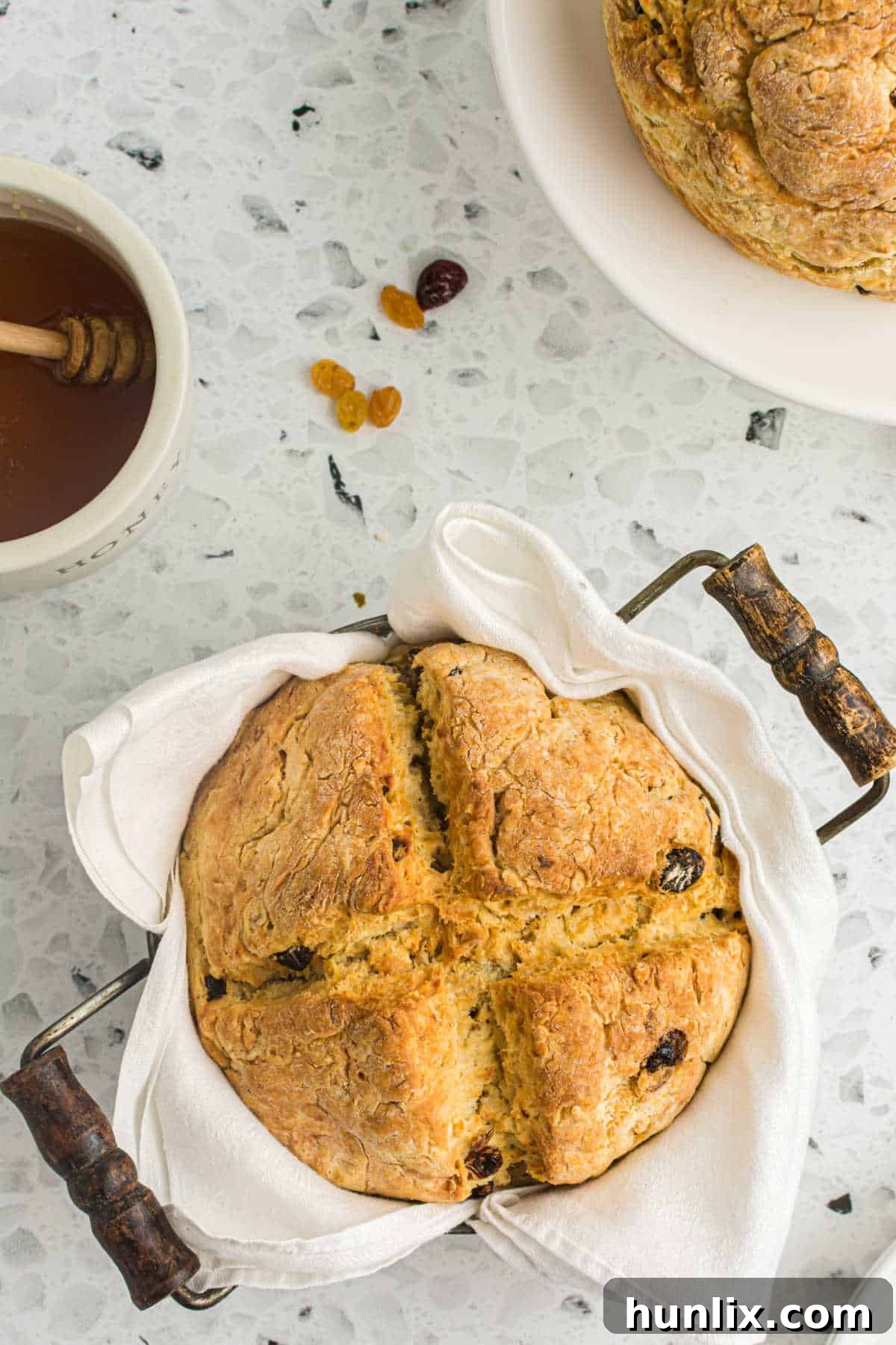 A freshly baked loaf of Irish Soda Bread still in its pan, resting on a white linen, showcasing its golden crust.