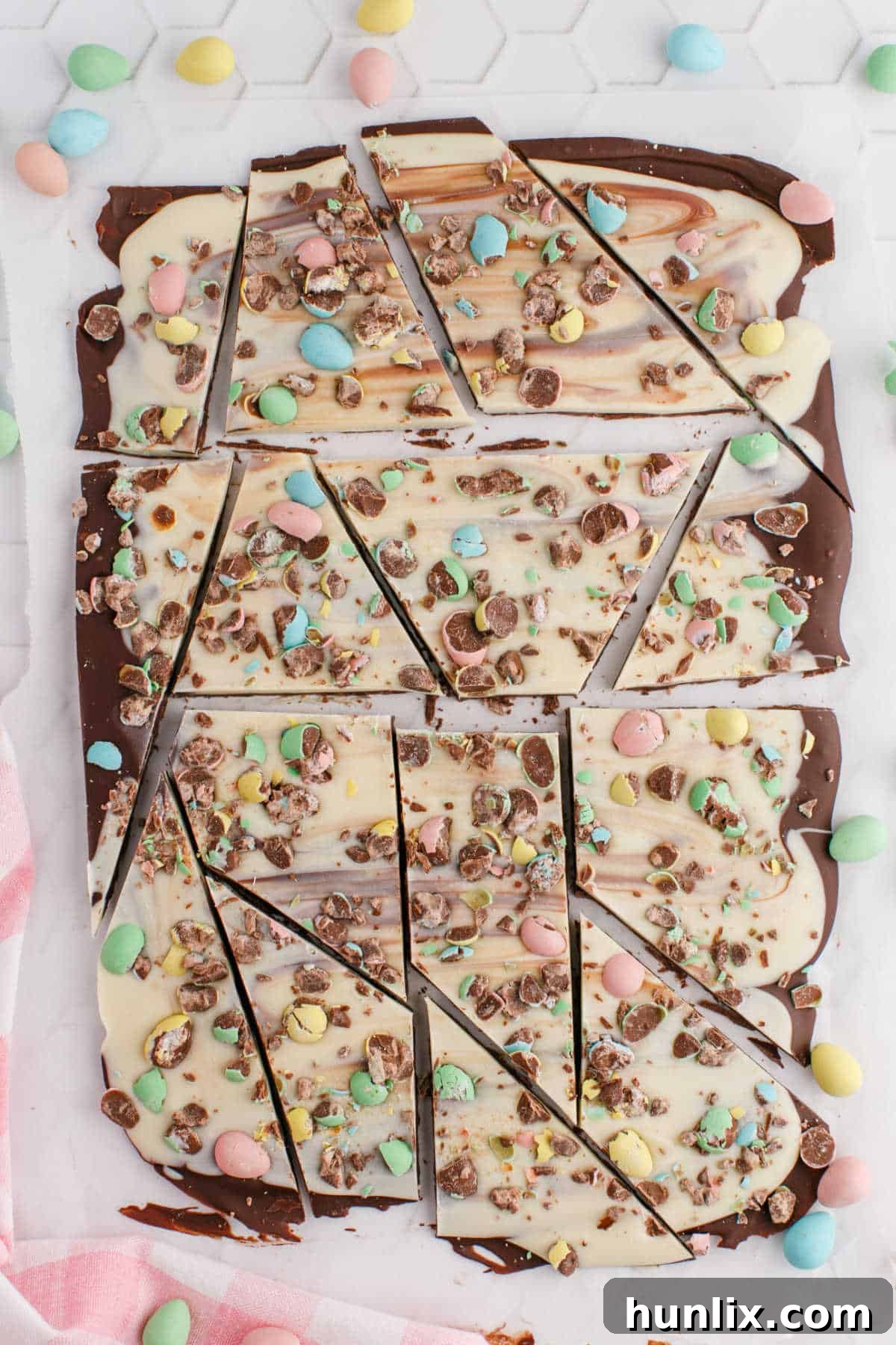 Delicious Easter bark with swirled chocolate and mini eggs, broken into pieces on a white surface, showcasing its vibrant layers and festive toppings.