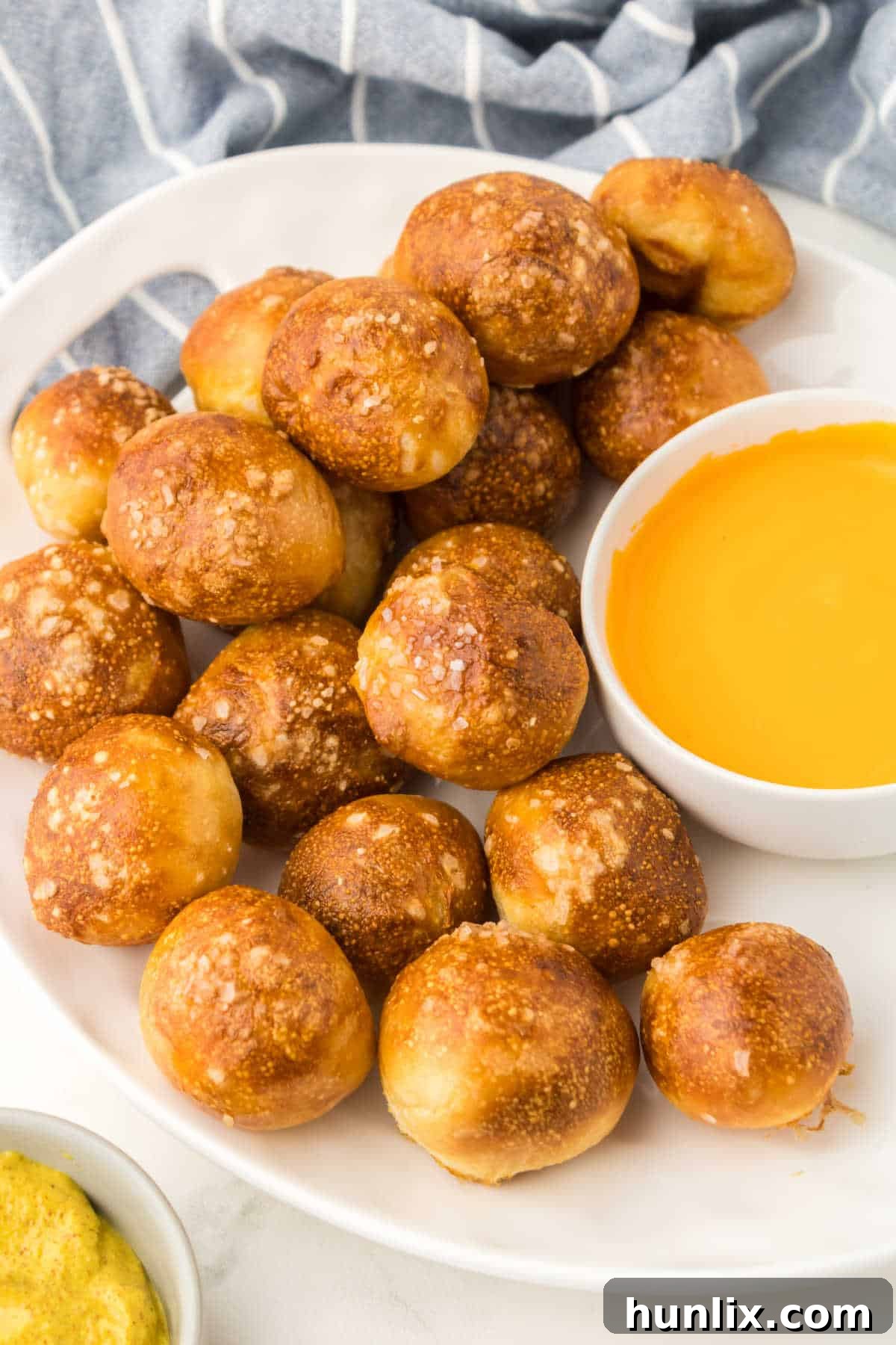 Golden Air Fryer Pretzel Poppers 7 A plate of air fryer pretzel bites with a bowl of cheese sauce next to it.