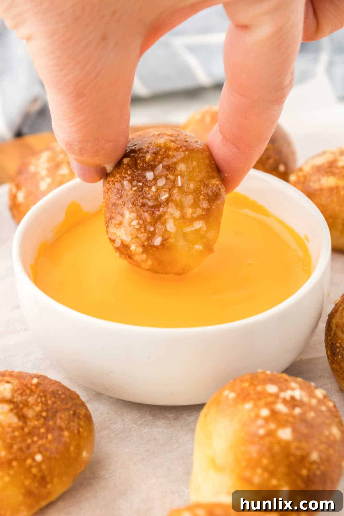 Golden Air Fryer Pretzel Poppers 9 A hand dipping an air fryer pretzel bite into a bowl of cheese sauce.