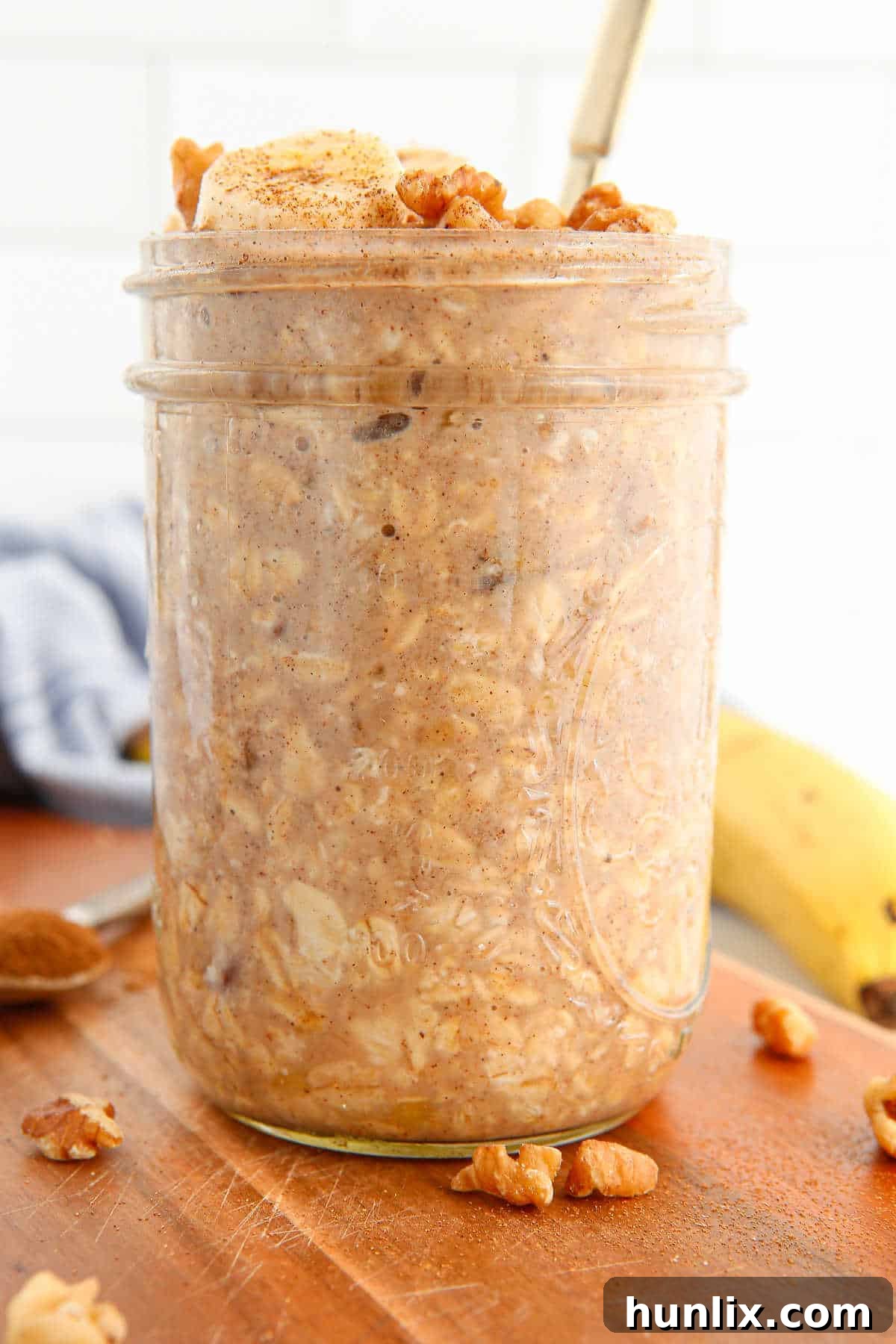 A mason jar of Banana Bread Overnight Oats with a spoon, ready to be eaten, set on a rustic wooden surface.