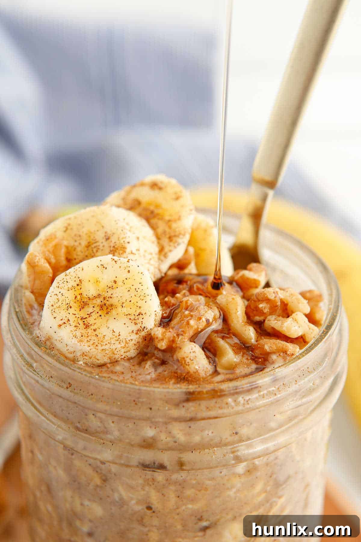 A mason jar of Banana Bread Overnight Oats, garnished with banana slices and a drizzle of maple syrup, ready to eat.