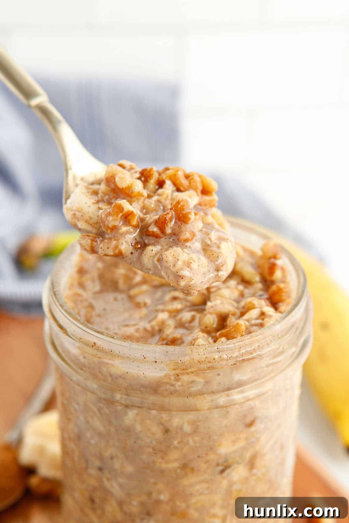 A close-up of a spoon lifting a scoop of Banana Bread Overnight Oats from a mason jar, highlighting the texture.