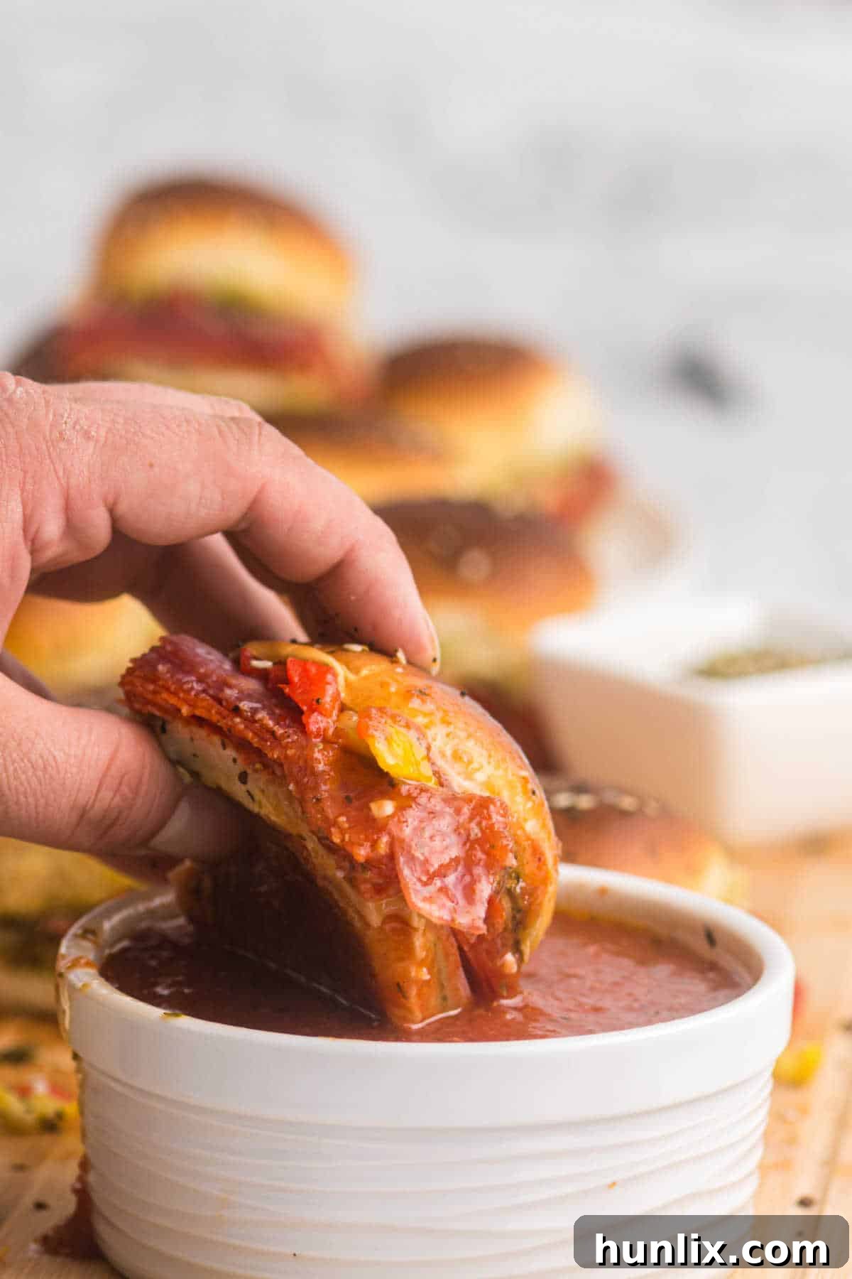A hand dipping a savory Italian slider into a bowl of marinara sauce.
