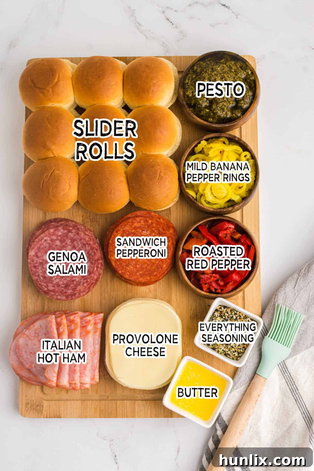 Assortment of ingredients laid out to make Italian sliders: rolls, pesto, cheeses, and various deli meats.