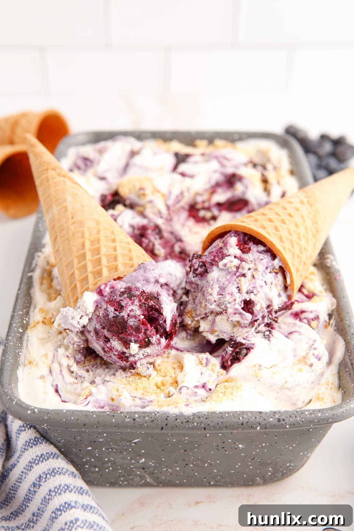 Two crispy ice cream cones nestled into a pan of rich, swirled blueberry pie ice cream, ready to be scooped and savored.