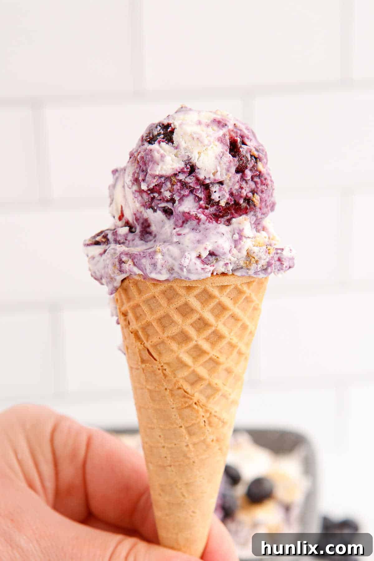 A perfectly scooped blueberry pie ice cream cone, glistening with creamy goodness and hints of blueberry, poised for a delicious bite.