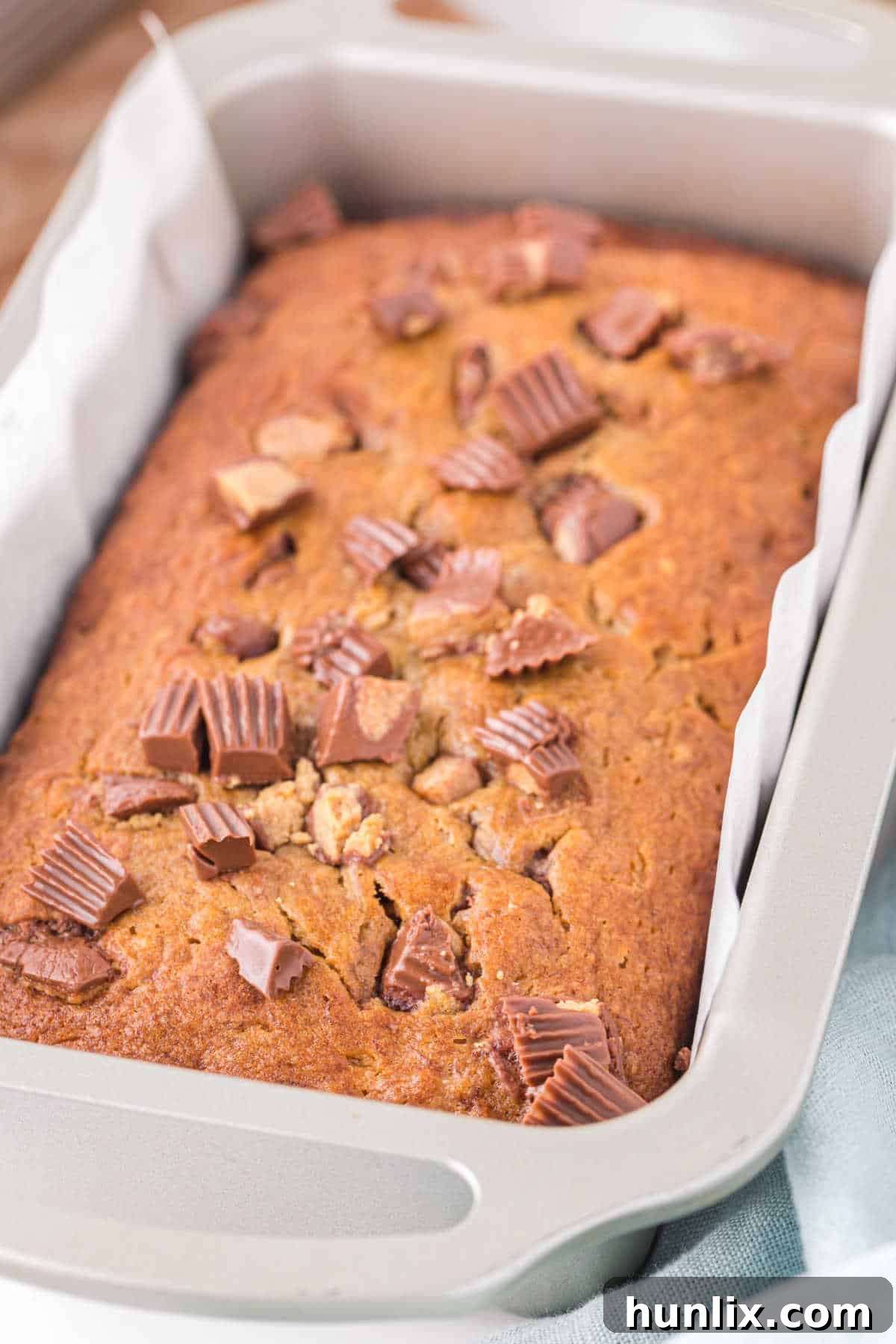 A freshly baked loaf of Reese's peanut butter banana bread in a loaf pan, showcasing its golden crust and chocolatey peanut butter cup chunks.
