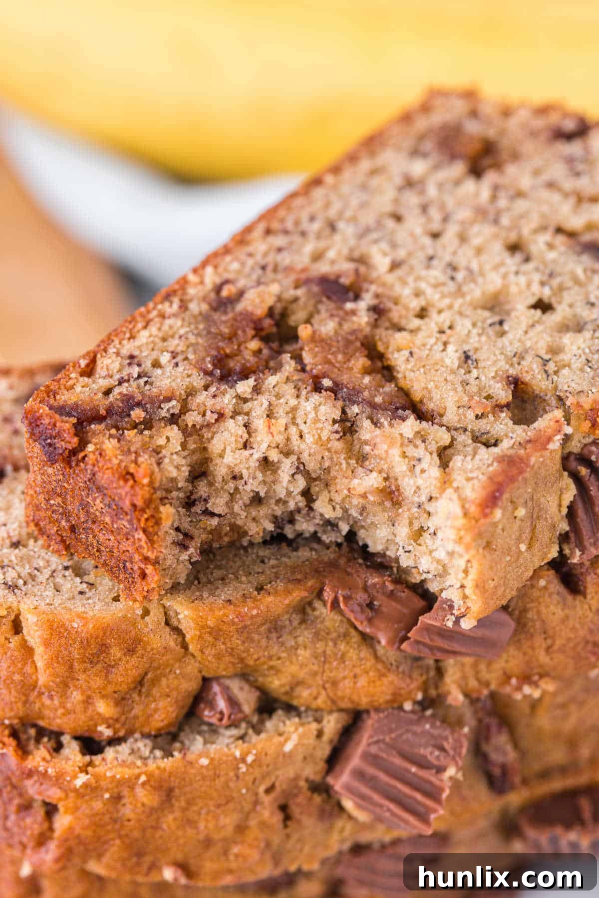 A stack of Reese's Peanut Butter Banana Bread slices on a plate, with a bite taken out of the top slice, showing the soft texture and peanut butter cup chunks.