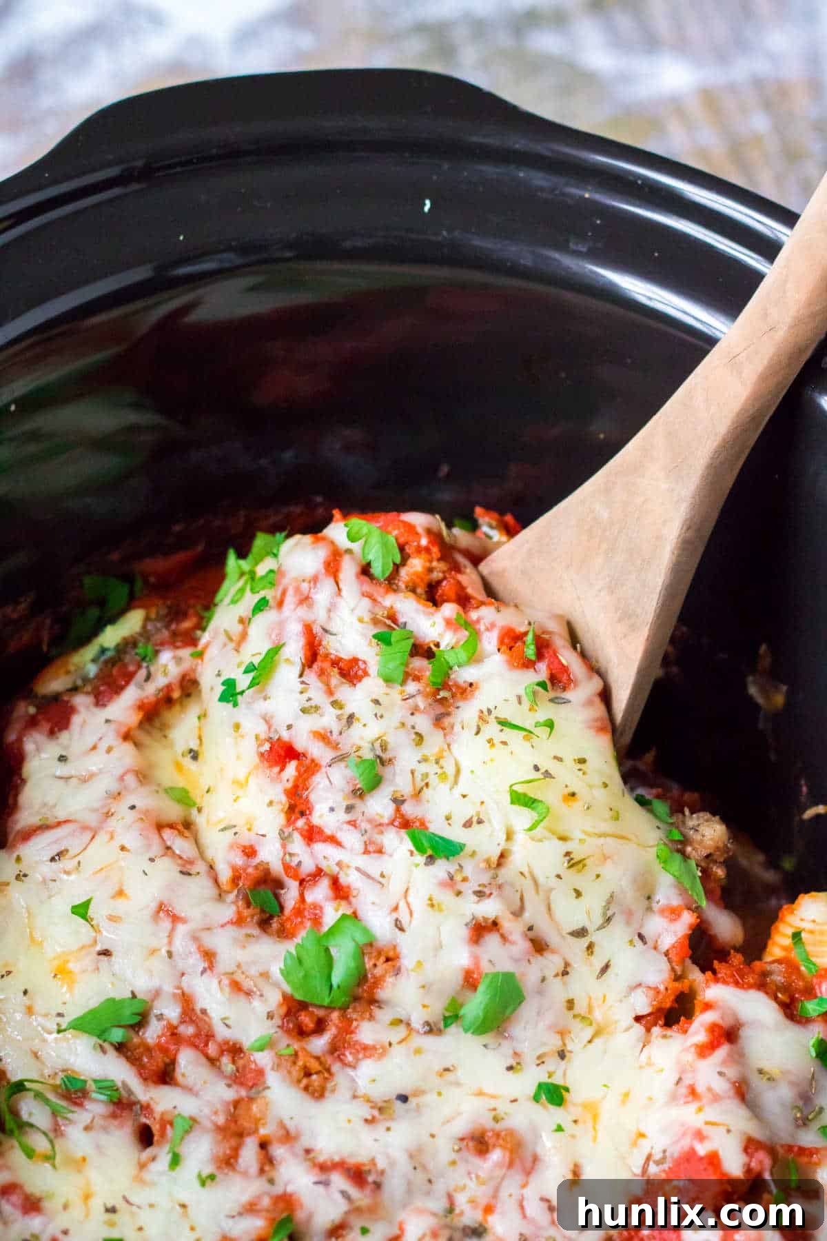 Stuffed shells in a crockpot with a wooden spoon.