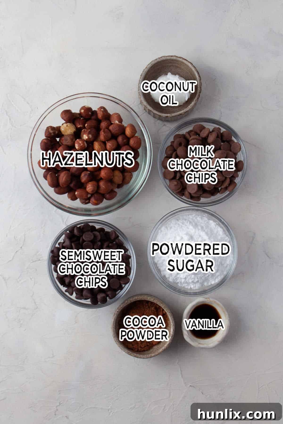 Decadent Homemade Chocolate Hazelnut Spread 3 A selection of ingredients laid out on a kitchen counter, including raw hazelnuts, powdered sugar, cocoa powder, vanilla extract, coconut oil, and both semi-sweet and milk chocolate.