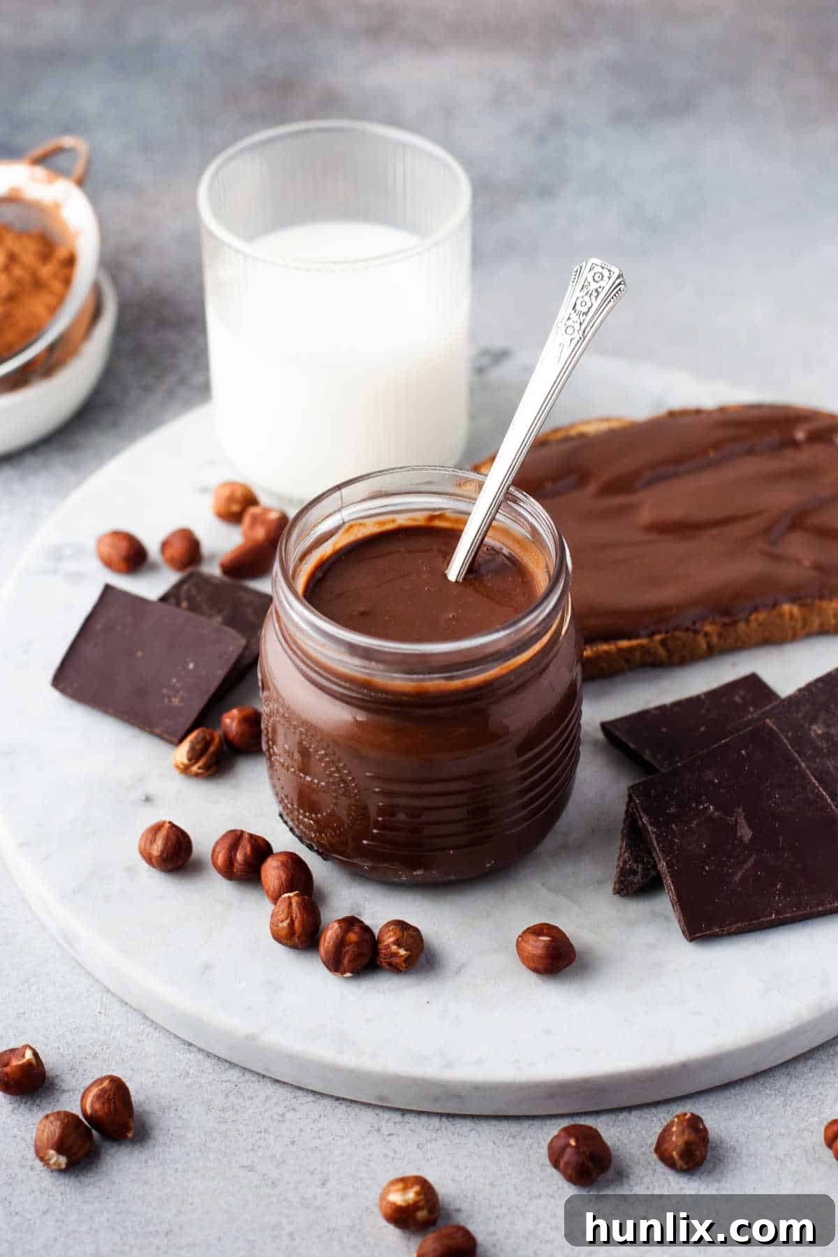 Decadent Homemade Chocolate Hazelnut Spread 9 A glass jar of homemade Nutella with a spoon sticking out, highlighting its creamy texture.