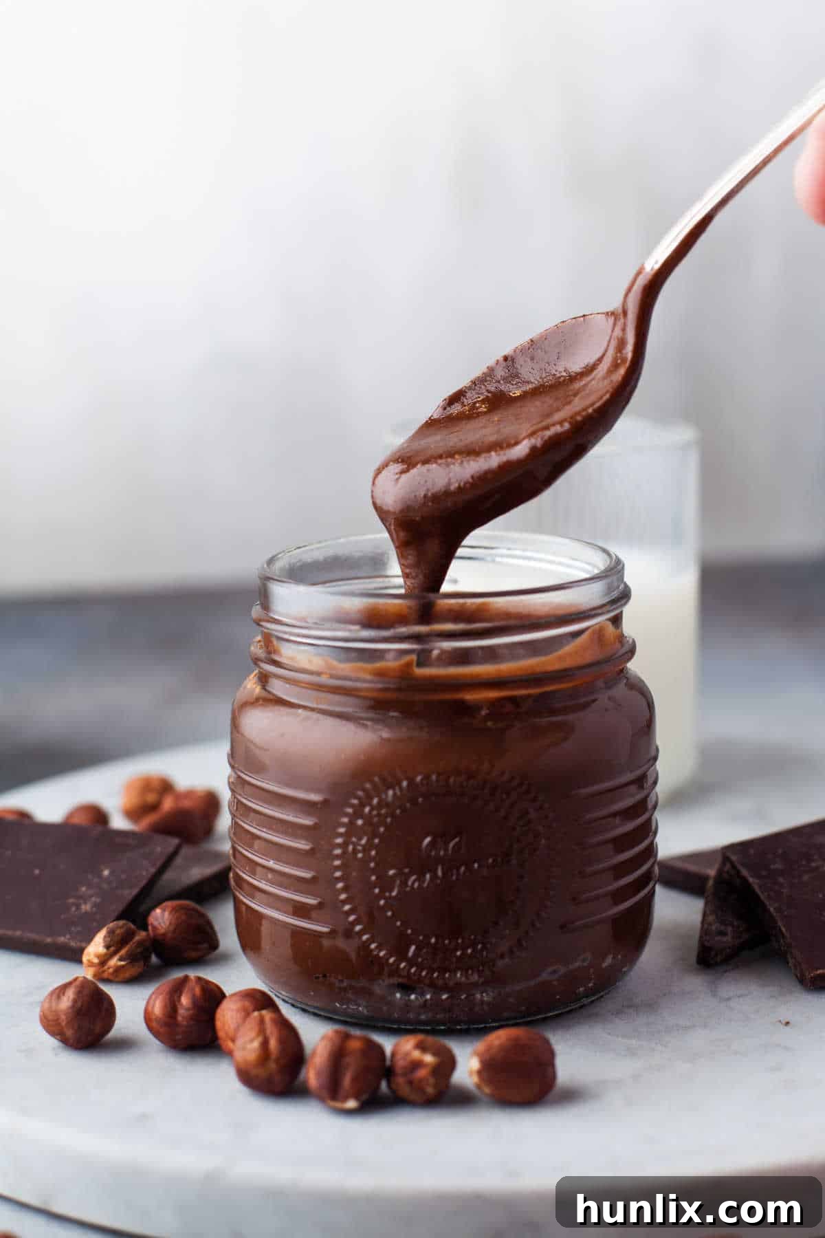 Decadent Homemade Chocolate Hazelnut Spread 10 A spoon overflowing with homemade Nutella held above a glass jar, demonstrating its rich, creamy texture.