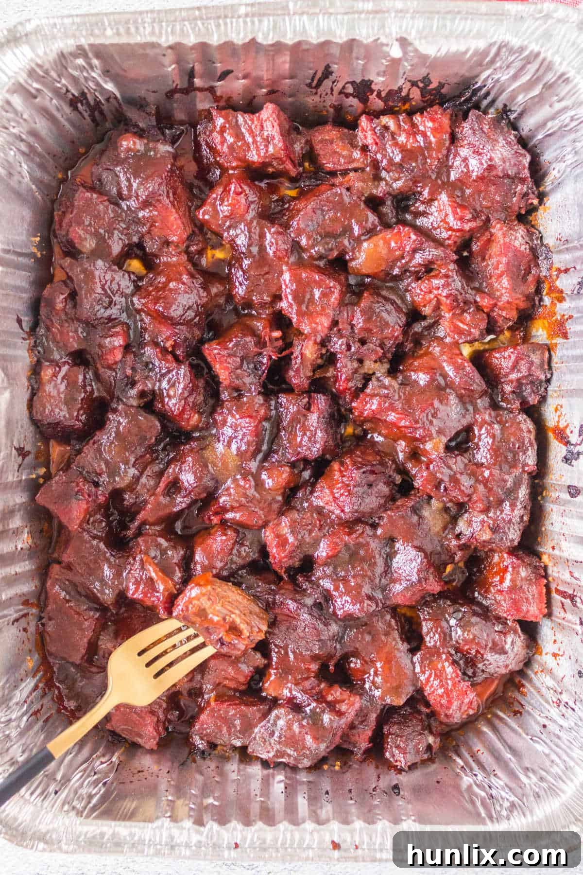 Perfectly smoked and sauced Poor Man's Burnt Ends in an aluminum pan, ready to be enjoyed.