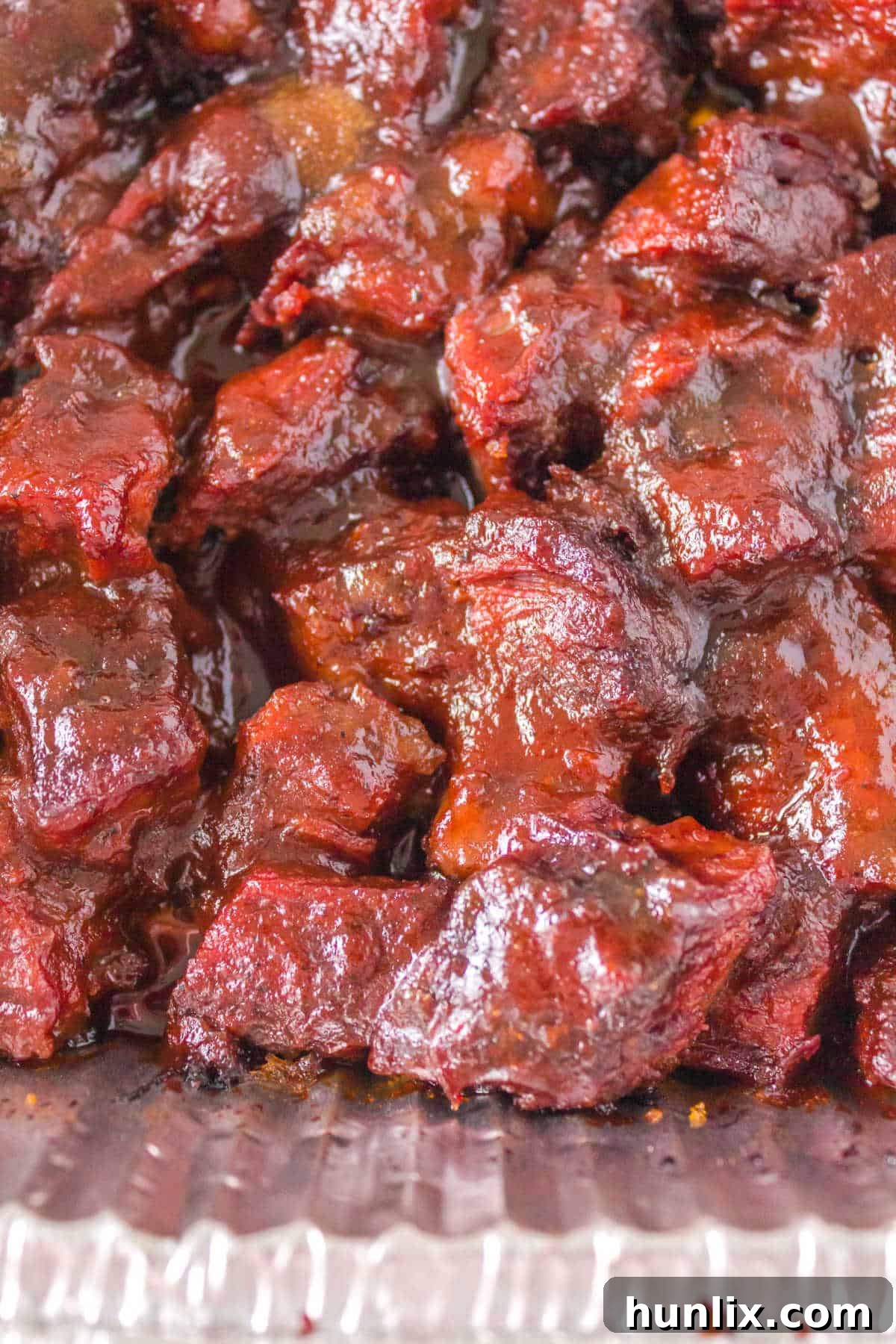 Close-up of Poor Man's Burnt Ends glistening with sauce in an aluminum pan.