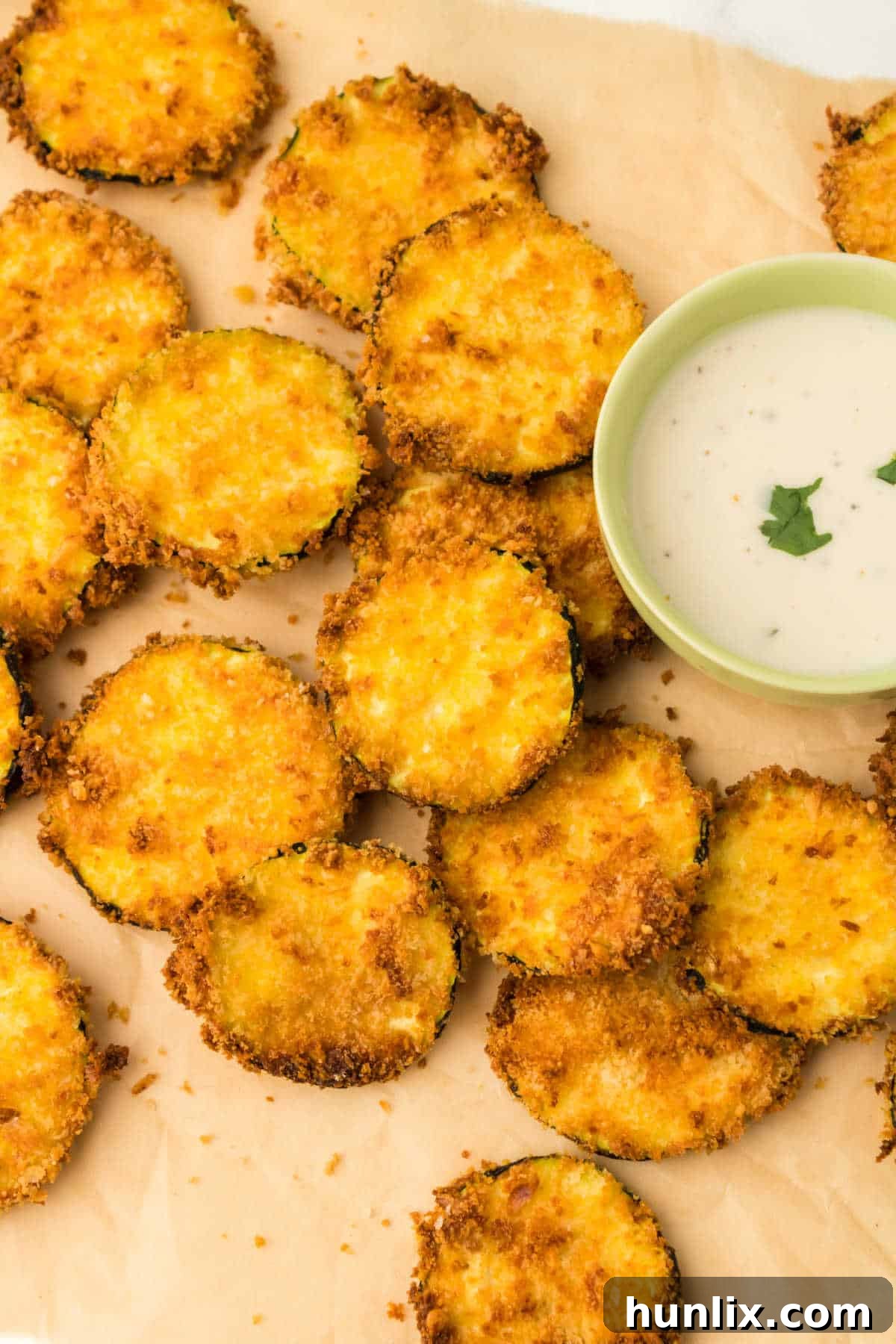 Golden Crispy Air Fryer Zucchini 8 Air fryer zucchini chips arranged on parchment paper with small bowls of dipping sauce.