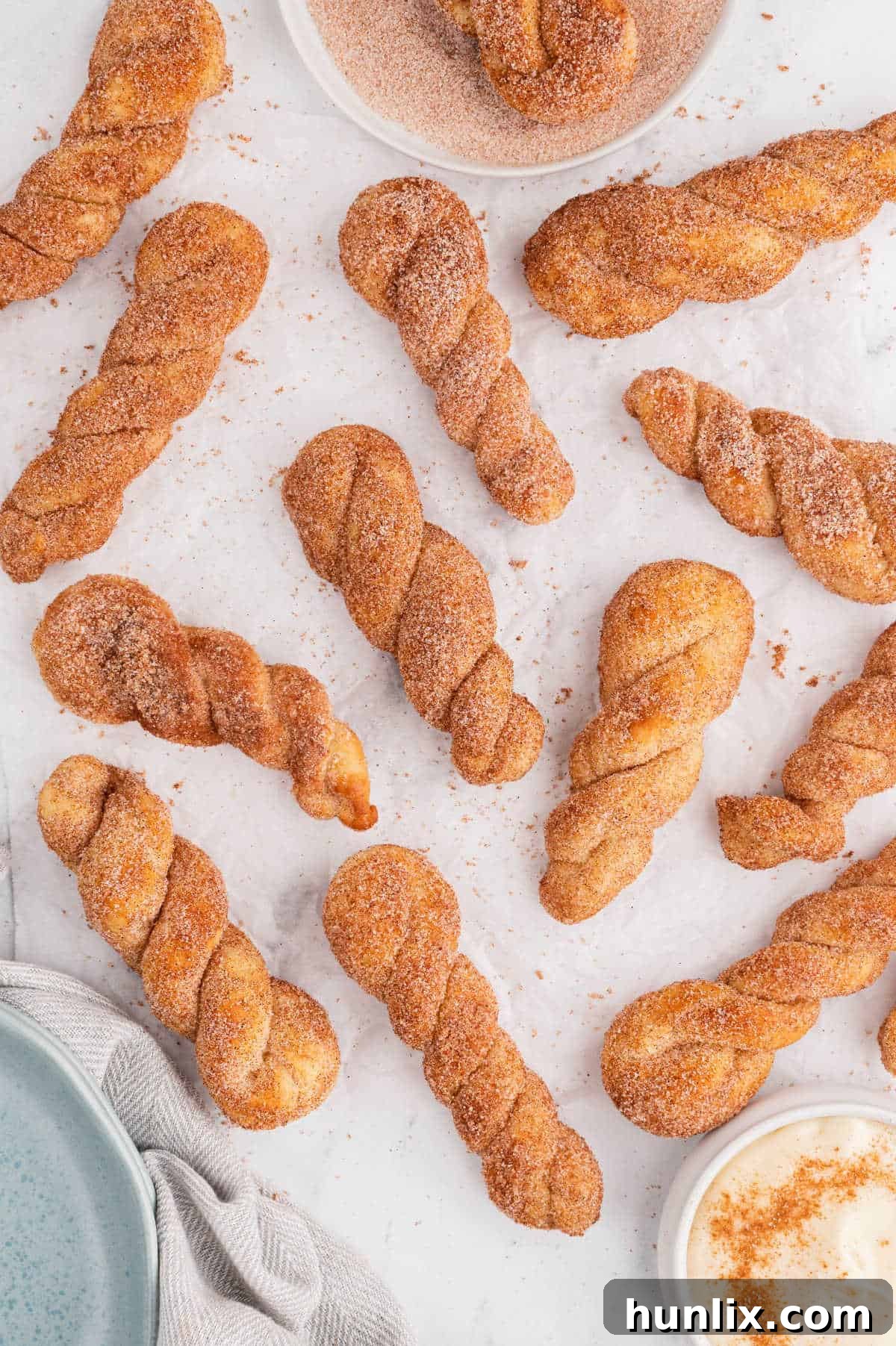 Air fryer cinnamon twists on a white surface with a bowl of cream cheese dip.