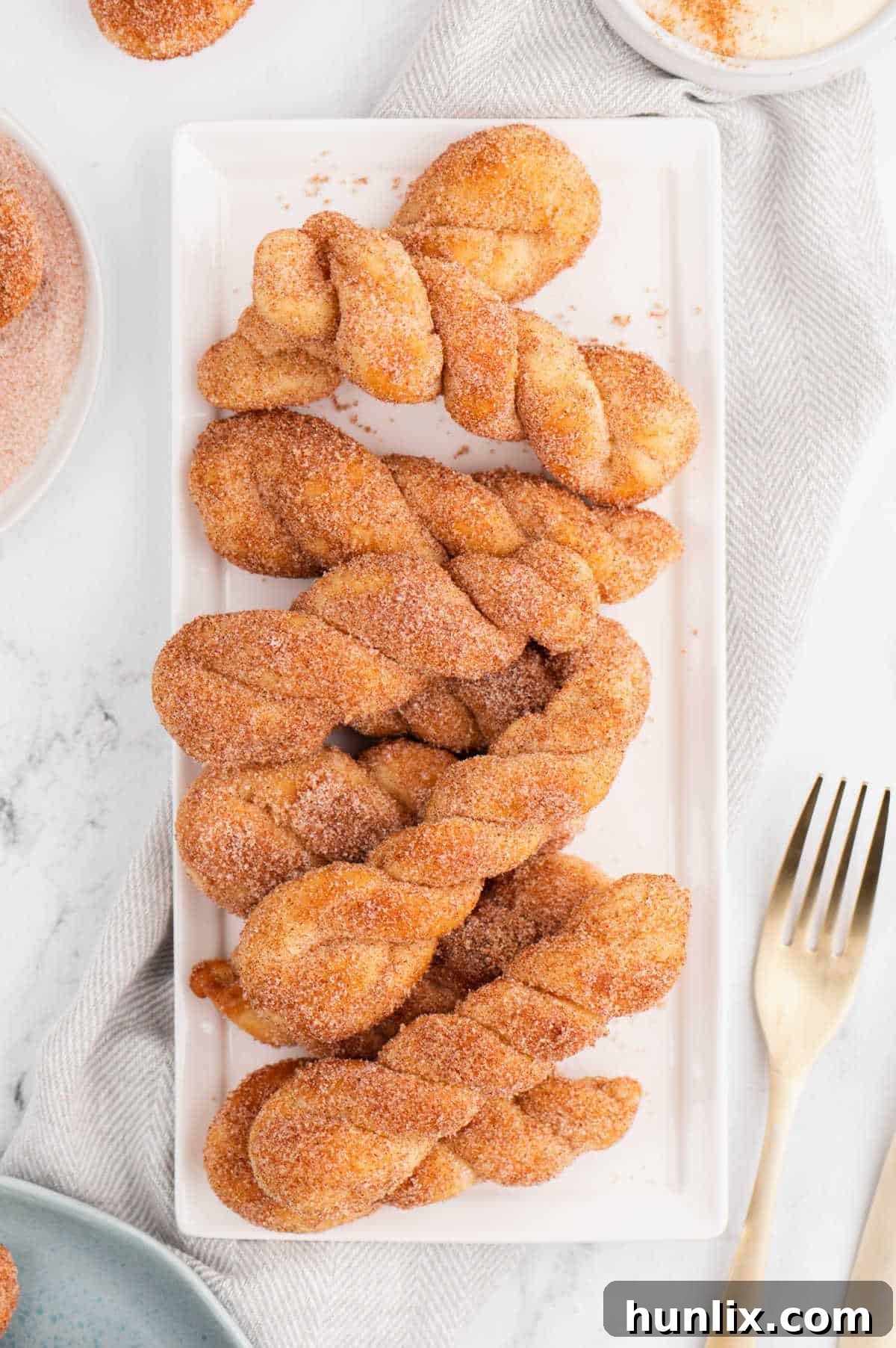 Air fryer cinnamon twists arranged on a white platter, showcasing their golden-brown finish.