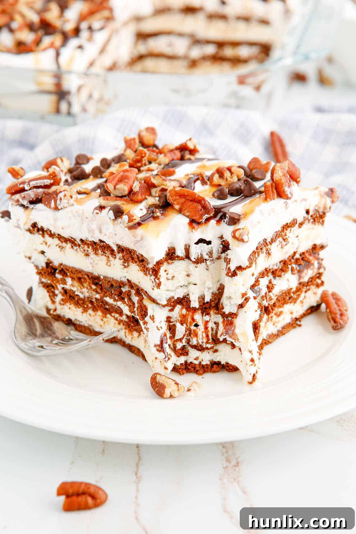 A slice of turtle ice cream sandwich cake on a plate with a bite out of it, showcasing the layers of ice cream sandwich, chocolate, caramel, and pecans.