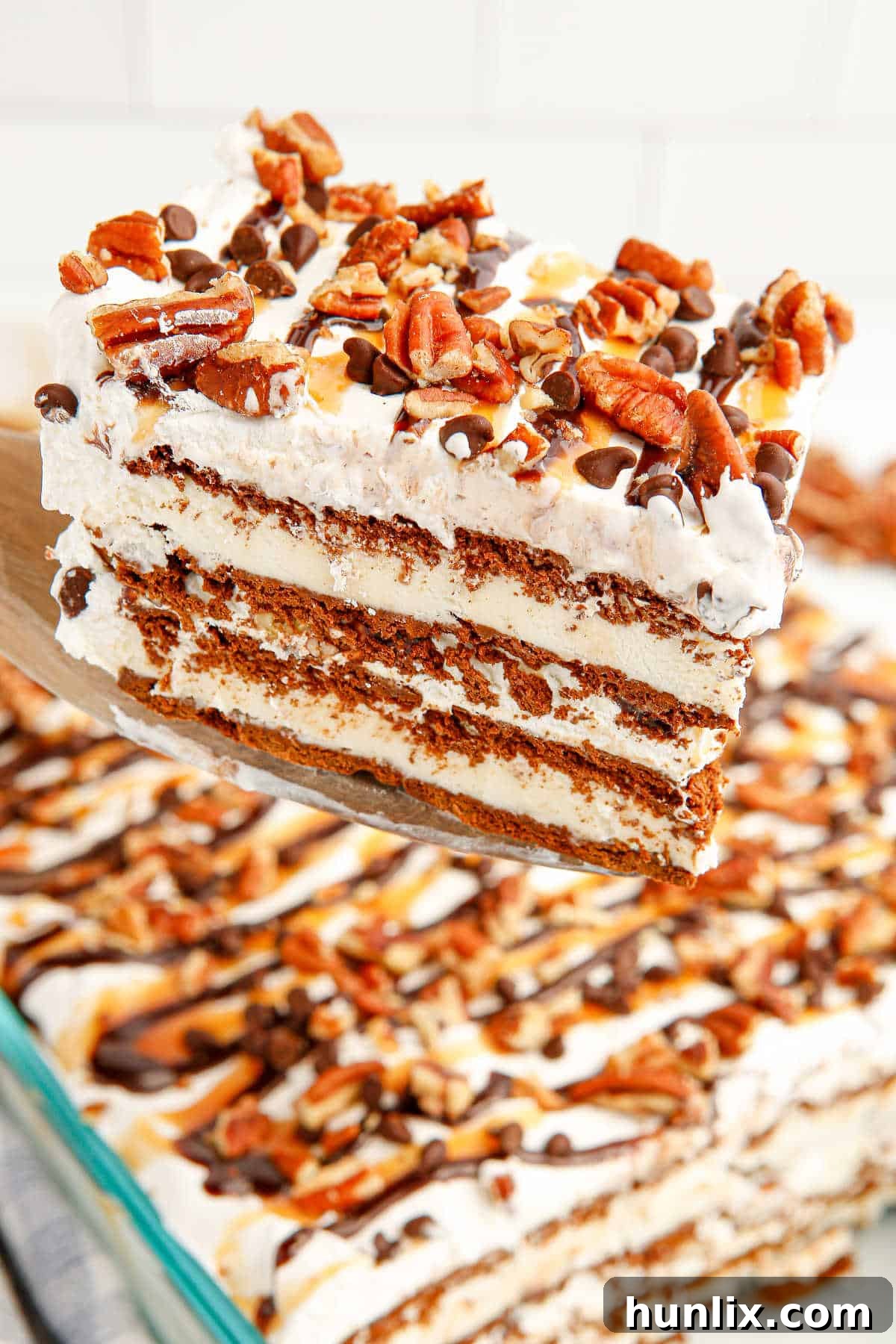 A large slice of Turtle Ice Cream Sandwich Cake being lifted from the pan with a cake server, highlighting its impressive layers.