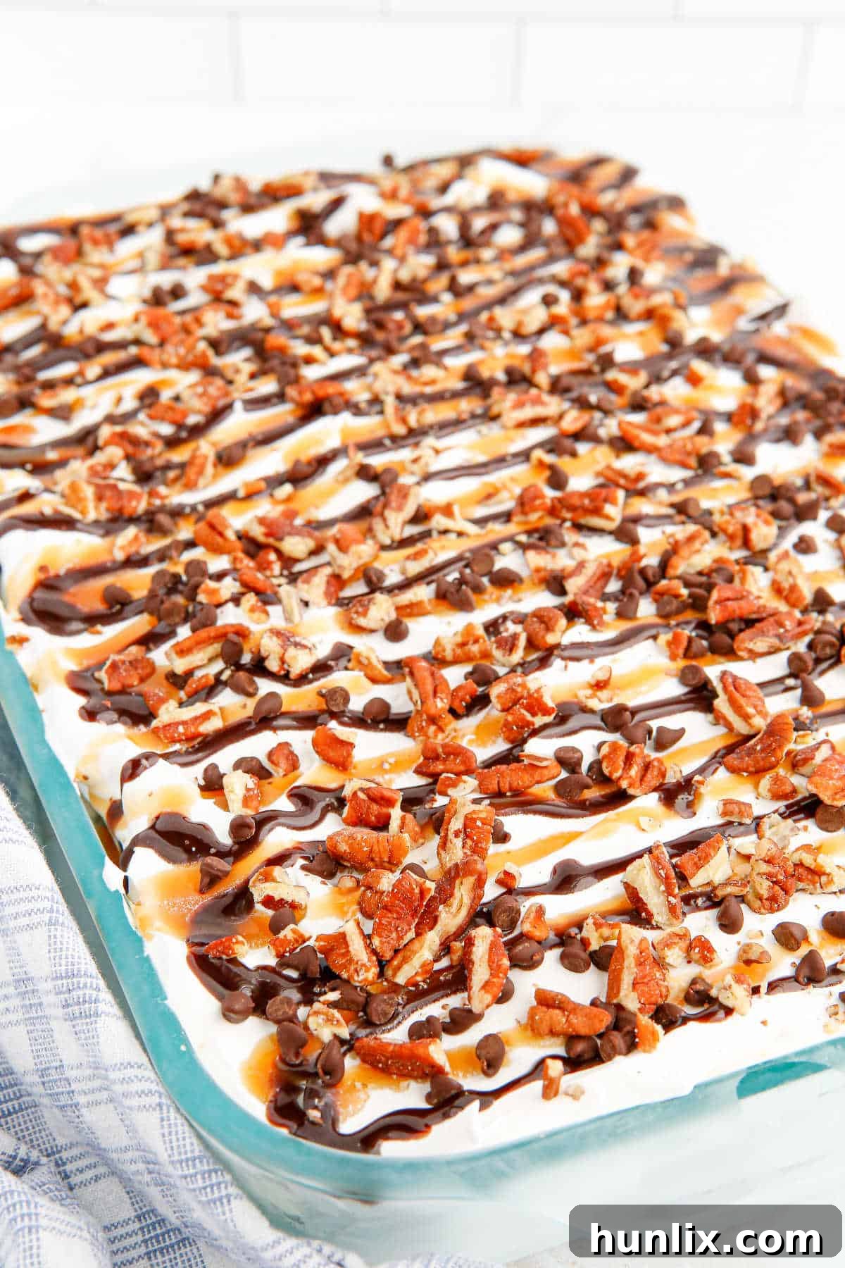 The entire Turtle Ice Cream Sandwich Cake, still in its baking pan, showcasing its finished top layer of sauces, pecans, and mini chocolate chips, ready for the freezer.
