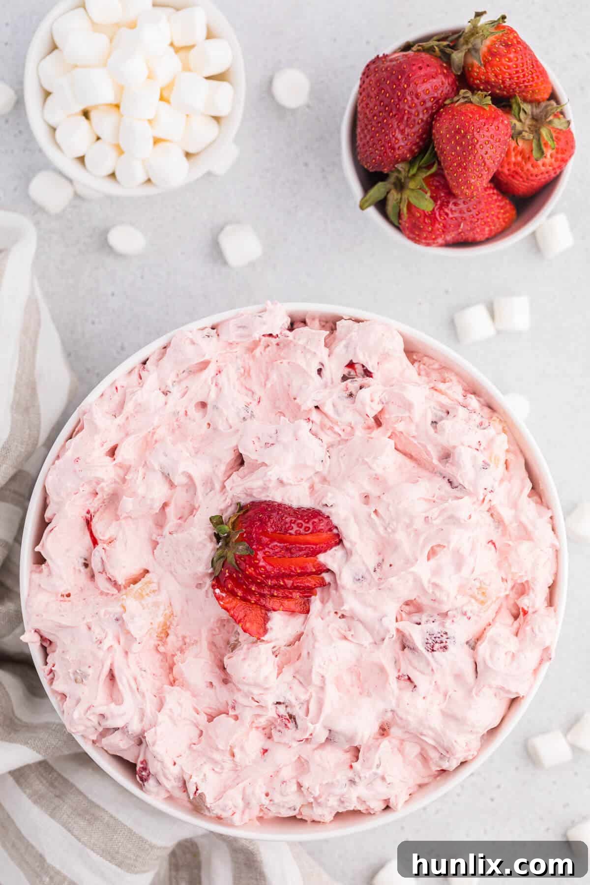 A white bowl of strawberry fluff salad, perfectly pink and garnished with fresh strawberries.