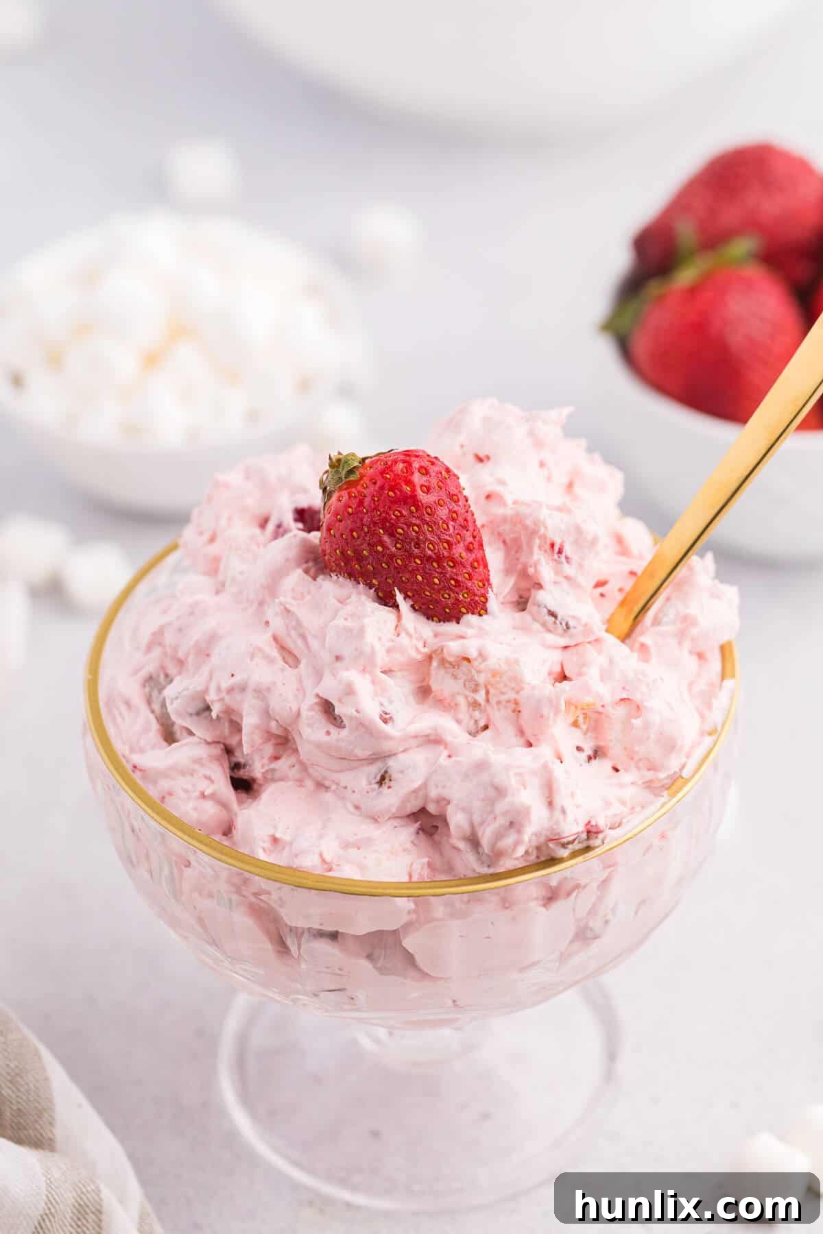 Strawberry fluff salad served in an elegant parfait dish with a spoon, showing layers of fluffy goodness.