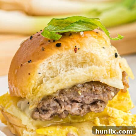 A single breakfast slider on a plate, showcasing its fluffy eggs, sausage, and melted cheese inside a sweet Hawaiian roll.