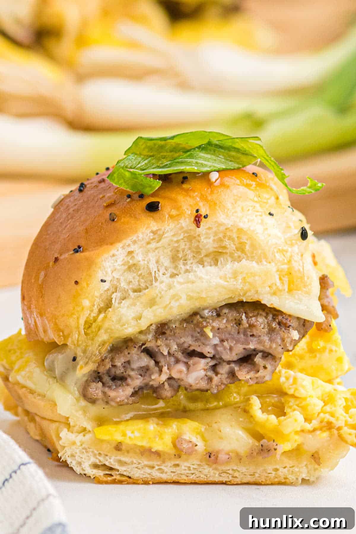 A single breakfast slider on a white plate, showcasing its layers of egg, sausage, and cheese within a Hawaiian roll.