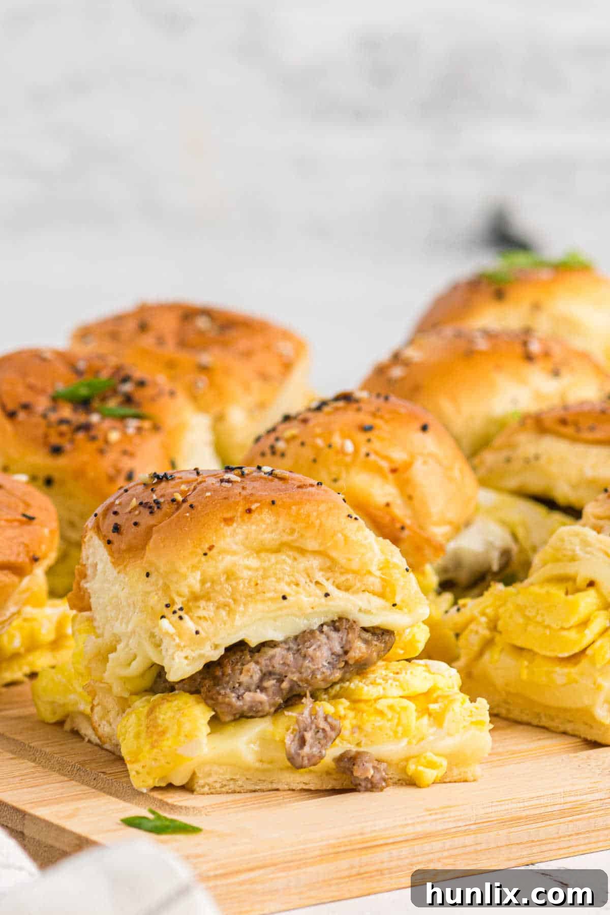 A group of breakfast sliders arranged on a wooden cutting board, showcasing their golden tops and delicious fillings.