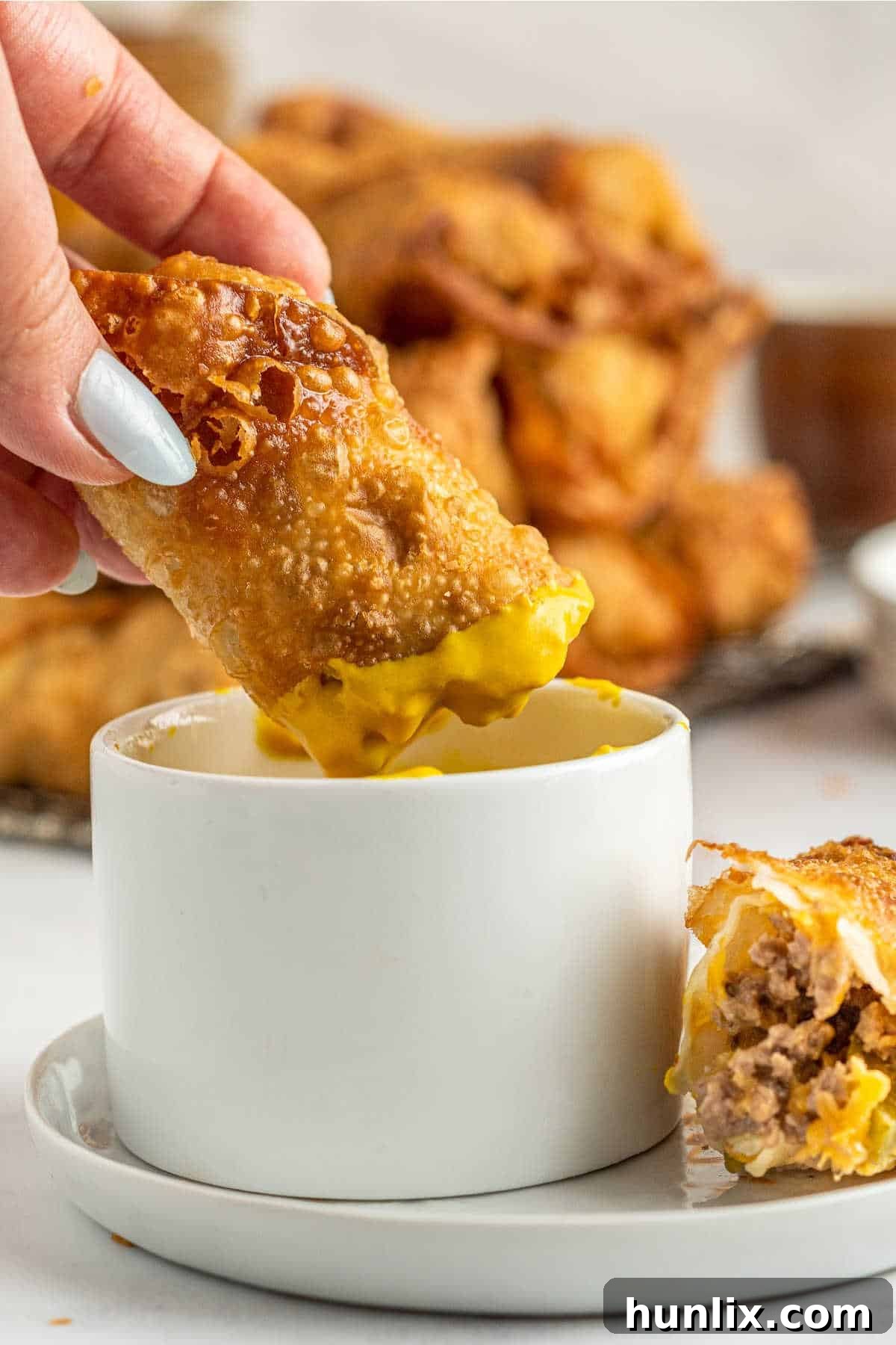 Crispy Cheeseburger Bundles 10 A hand dipping a cheeseburger egg roll in a dish of mustard.