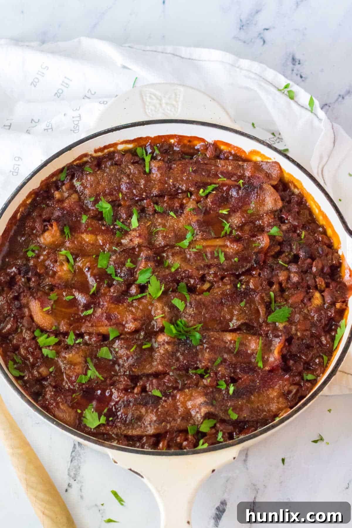 A large pot brimming with rich, homemade baked beans, generously mixed with ground beef and topped with crispy bacon.