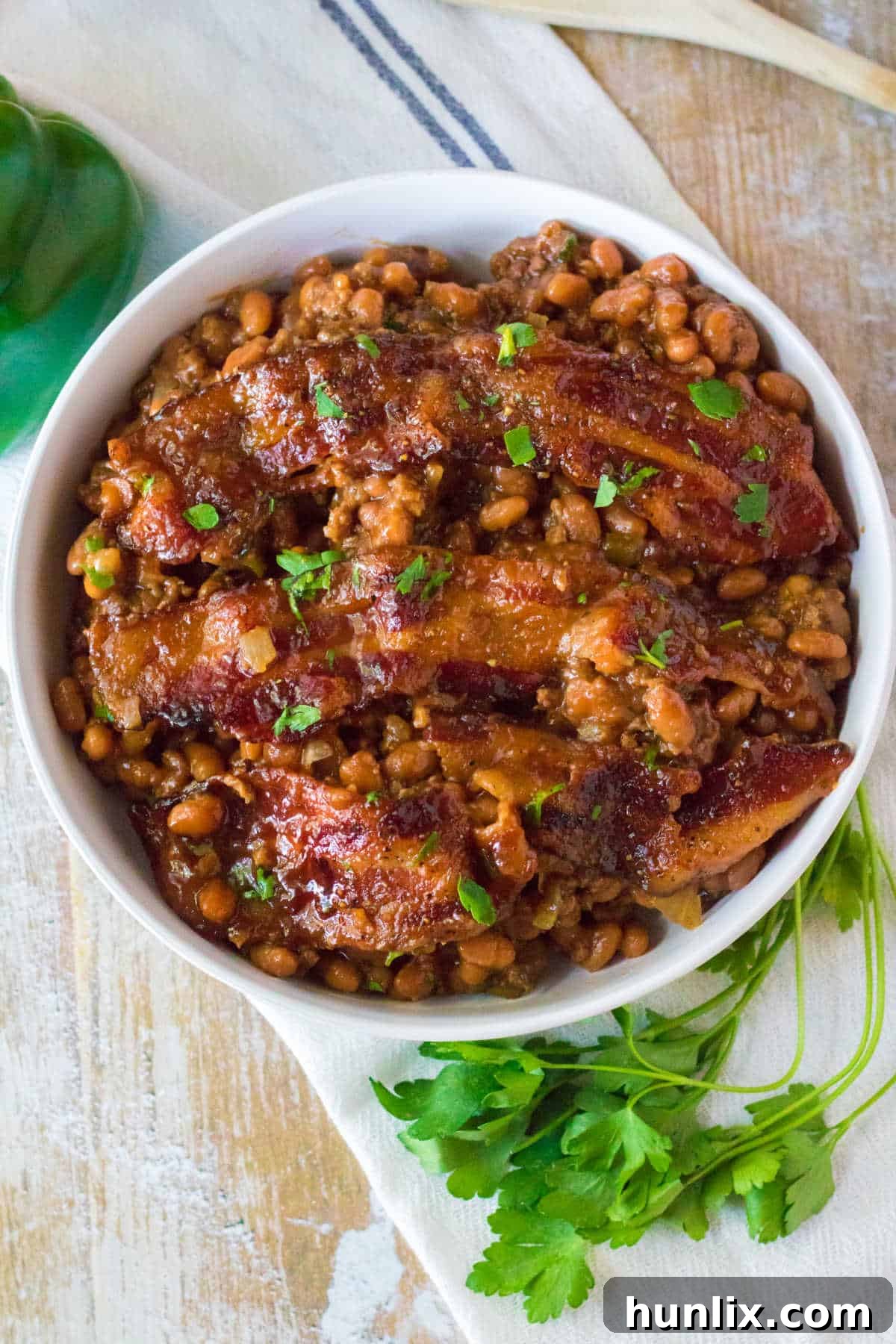 A single serving of baked beans with ground beef and bacon, garnished with fresh parsley, in a white bowl.