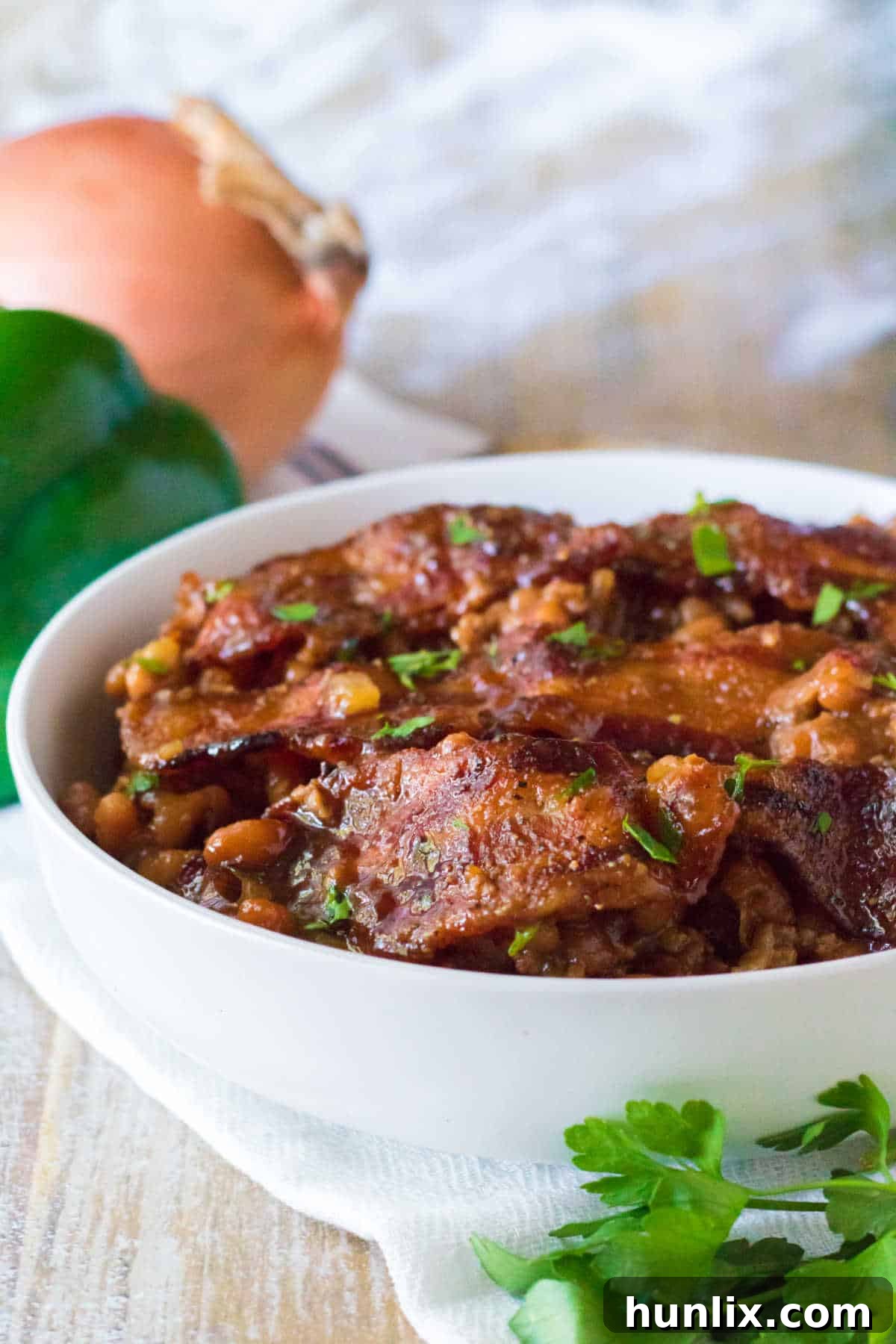 Two white bowls filled with hearty baked beans with ground beef, garnished with fresh herbs, ready for serving.