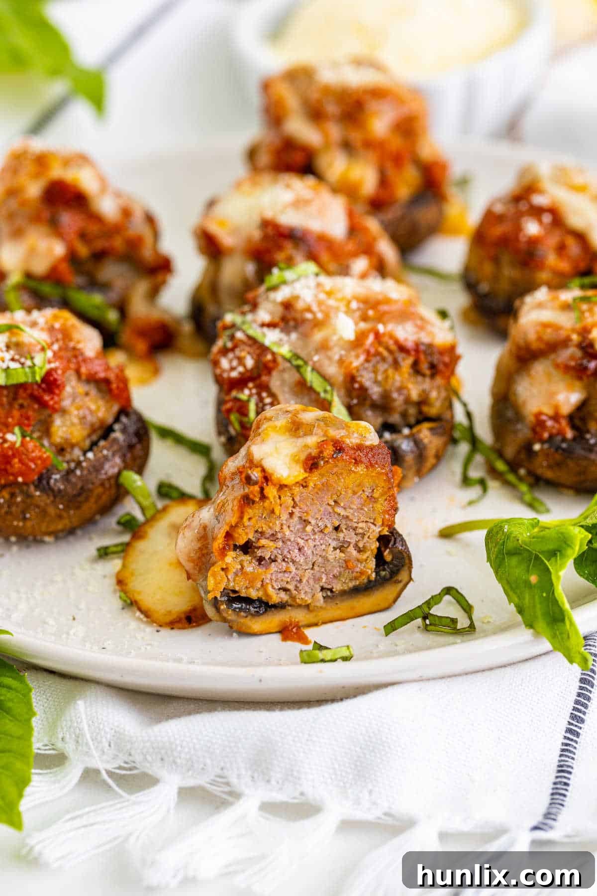 A close-up of a meatball stuffed mushroom, cut in half to reveal the perfectly cooked meatball, marinara, and melted cheese inside.