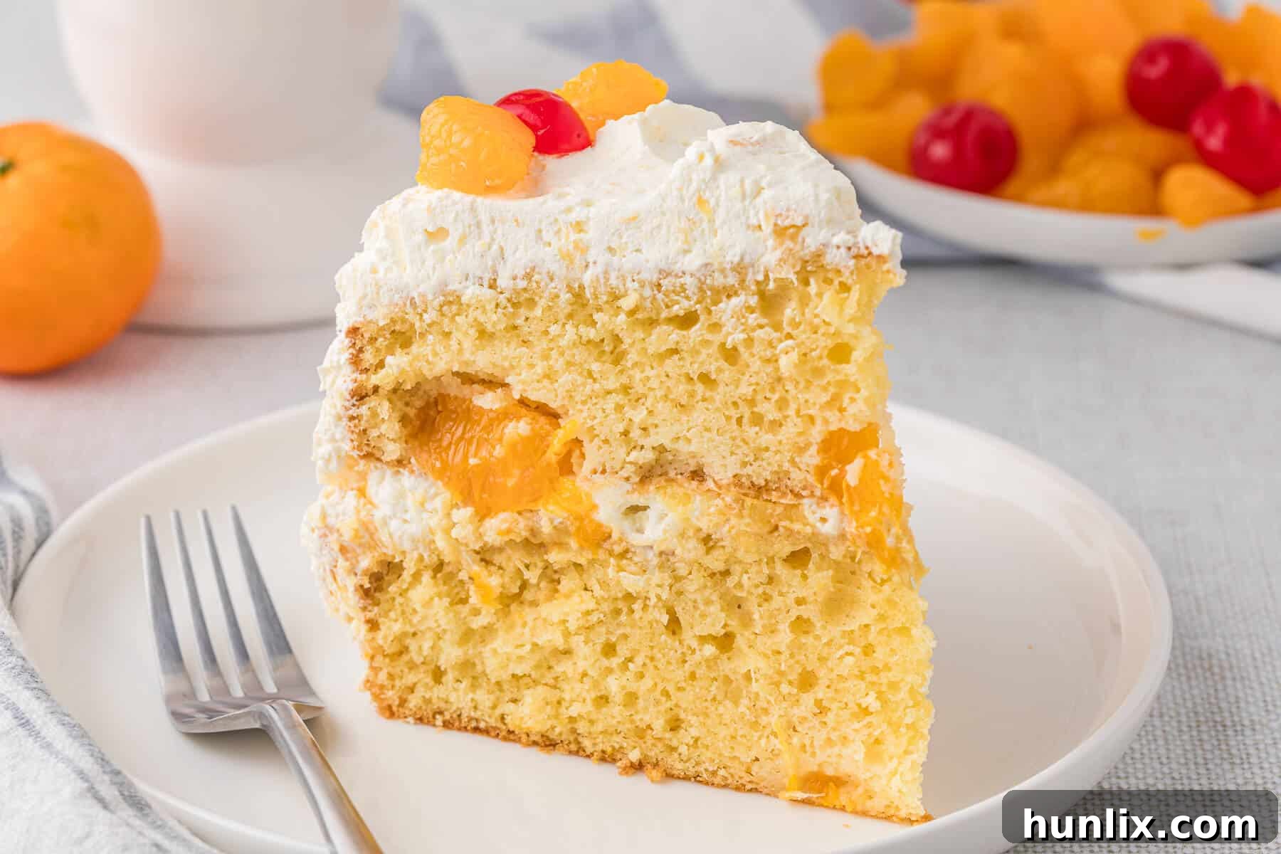 Sunshine Citrus Cloud Cake 10 A close-up shot of a slice of Pig Pickin' Cake on a plate, highlighting the airy texture of the cake and the creamy frosting, with a fork poised to take a bite.