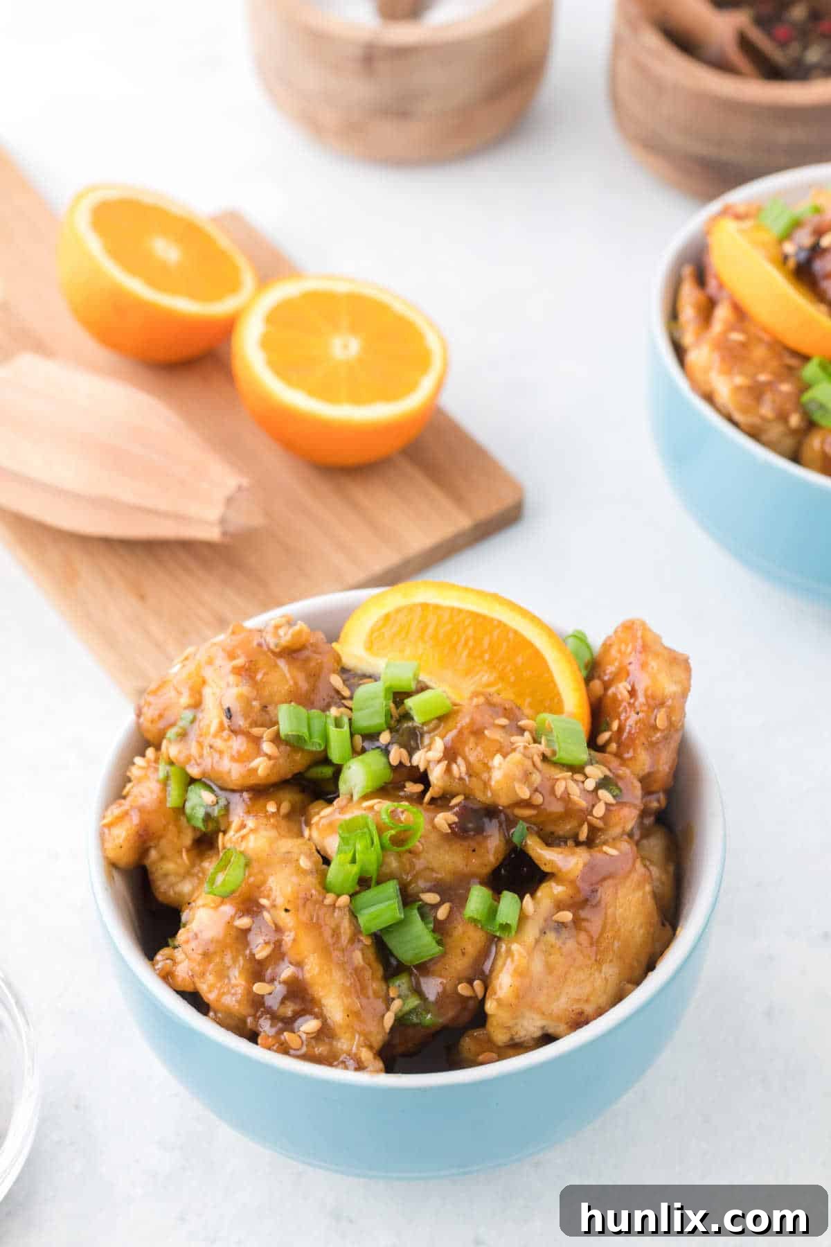 Orange chicken in a vibrant blue bowl, garnished with fresh green onions and sesame seeds, showcasing its crispy texture and glossy sauce.