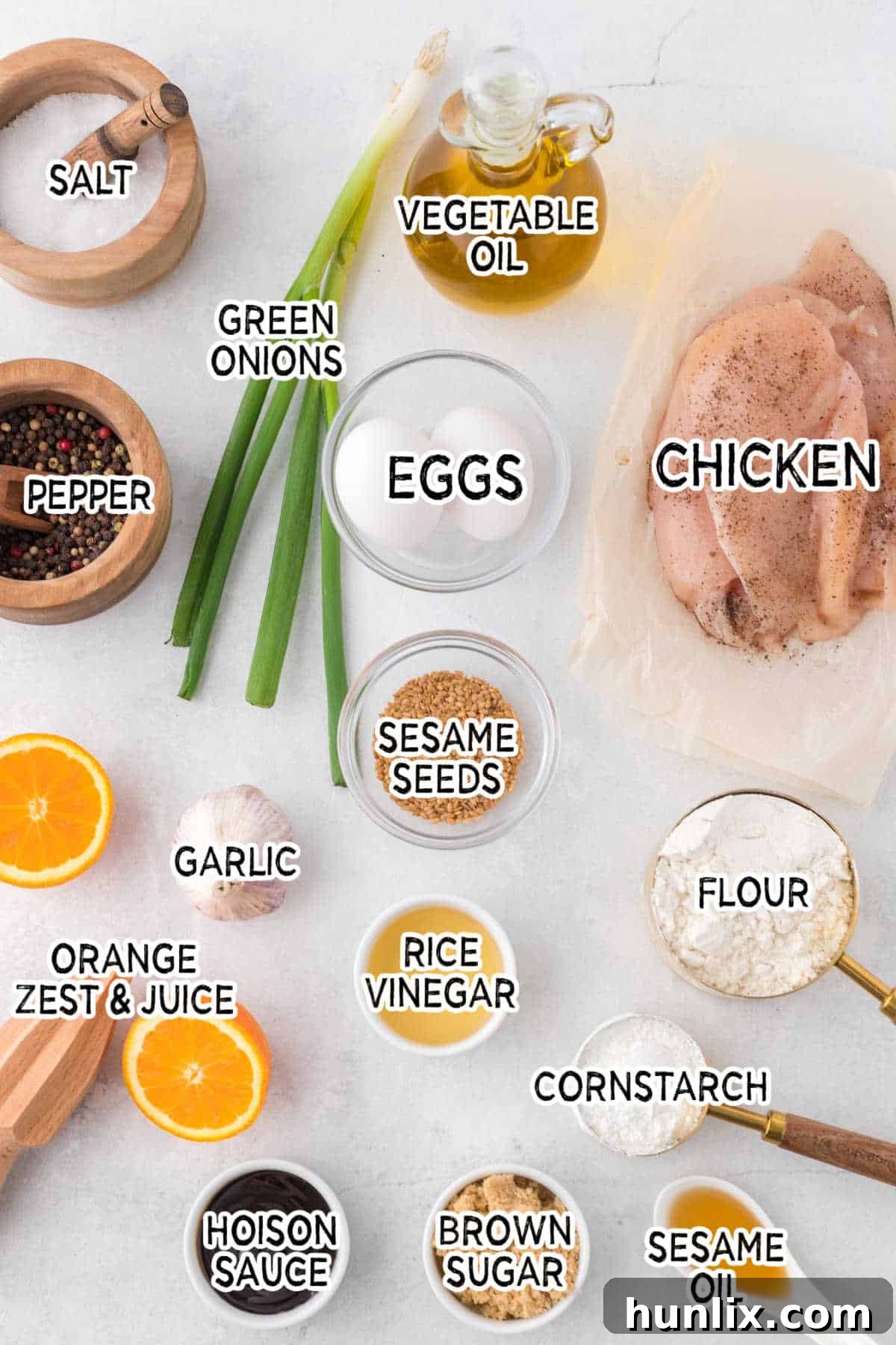 A colorful array of ingredients arranged on a wooden board, including fresh oranges, chicken breast, eggs, and various condiments, ready for orange chicken preparation.