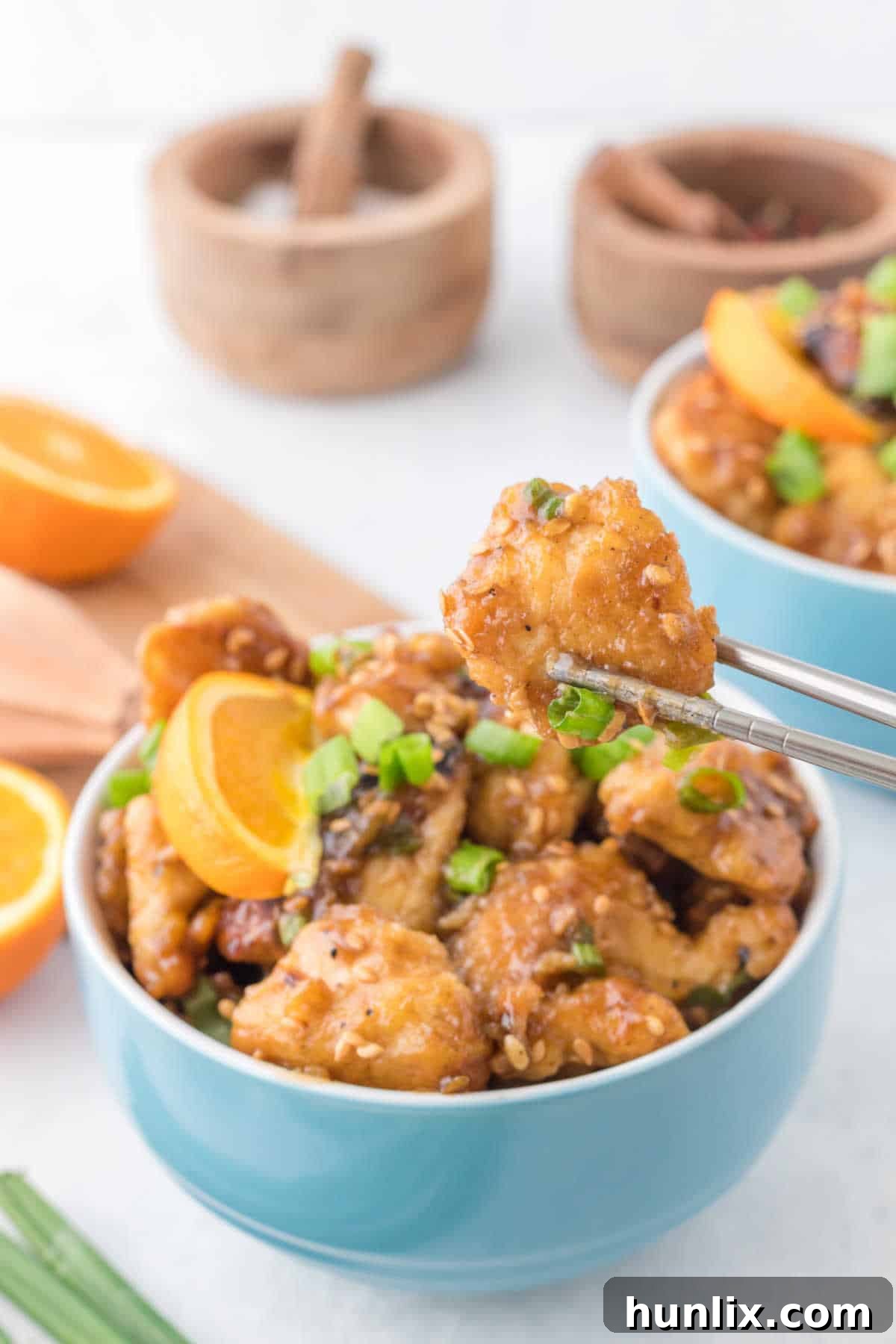 A single piece of perfectly glazed orange chicken held delicately by chopsticks, highlighting its appetizing texture and vibrant color.