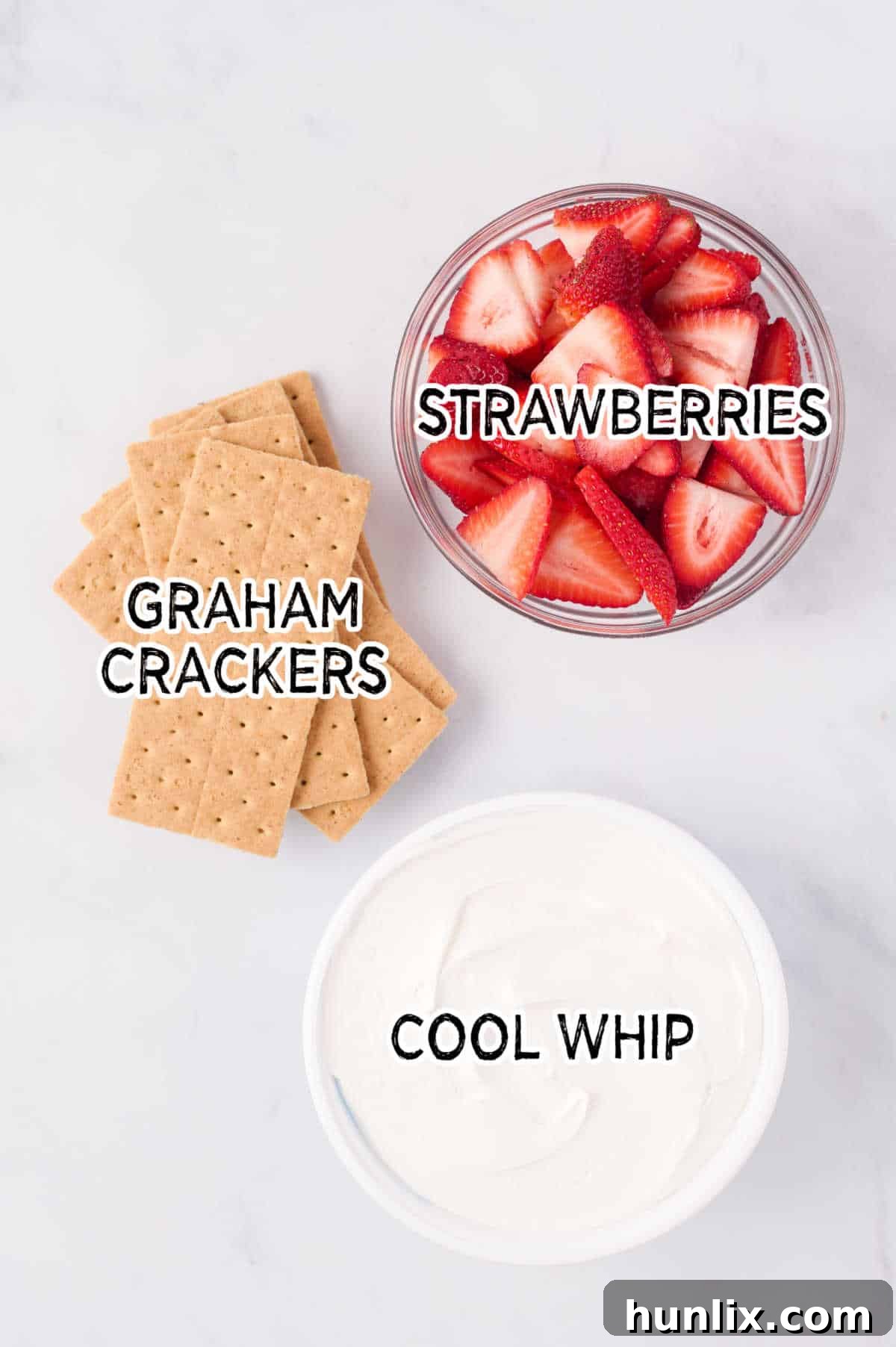 Fresh graham crackers, a tub of Cool Whip, and sliced strawberries laid out on a white background, representing the simple ingredients.