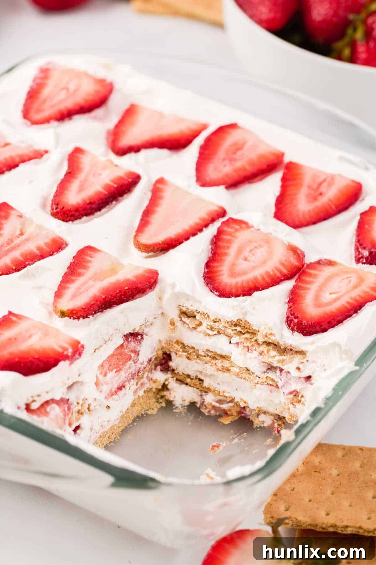 A pan of the freshly chilled strawberry icebox cake with a piece already cut out, revealing the beautiful layers.