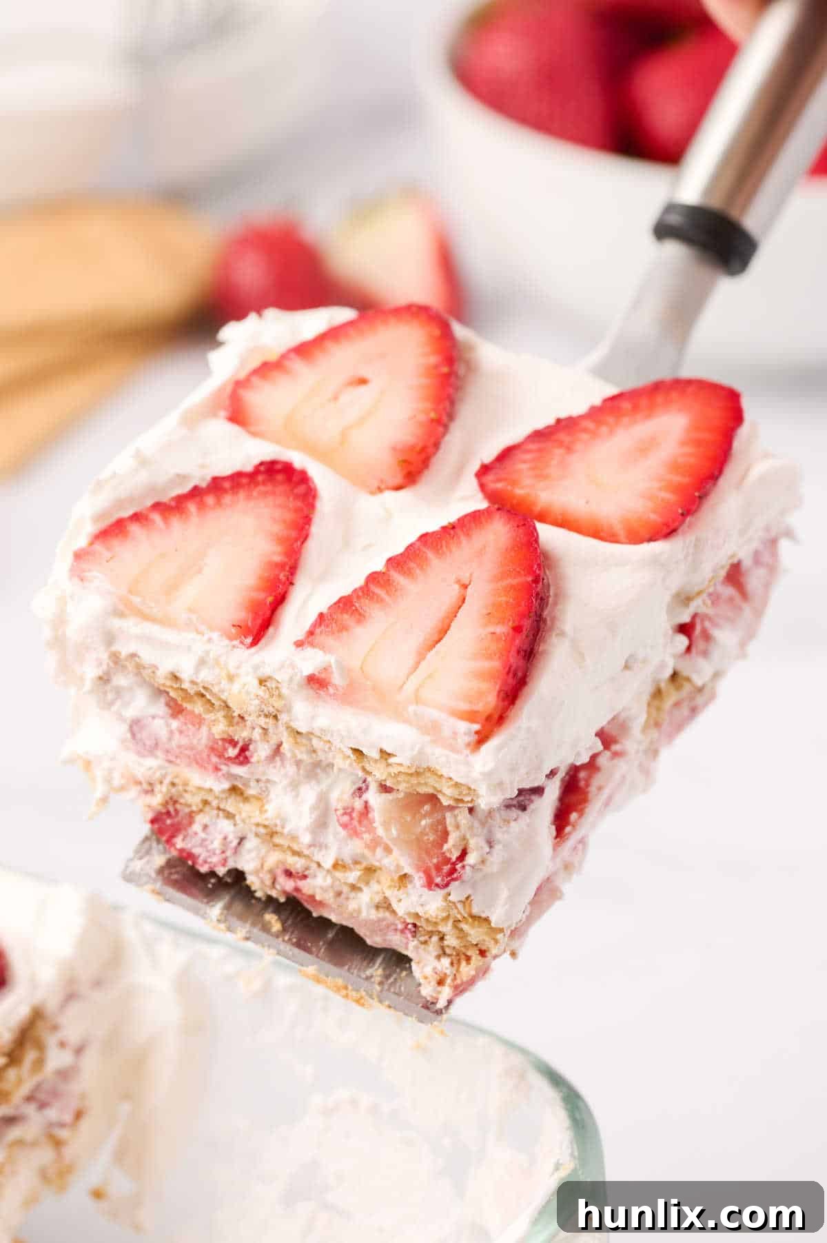 A serving spatula lifting a perfect slice of strawberry icebox cake out of the pan.