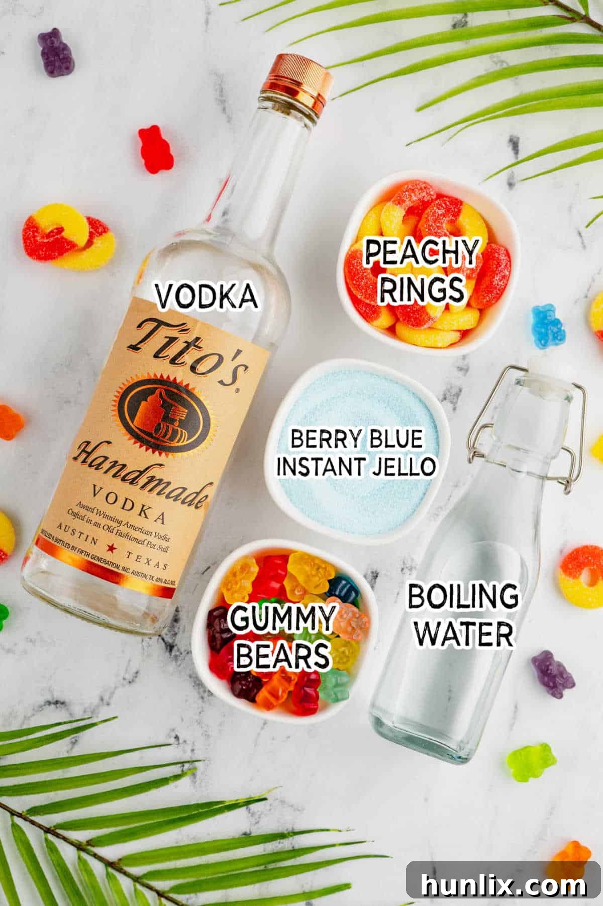 A vibrant display of ingredients for making Pool Party Jello Shots, including blue jello packets, vodka, gummy bears, and peach rings on a white background.