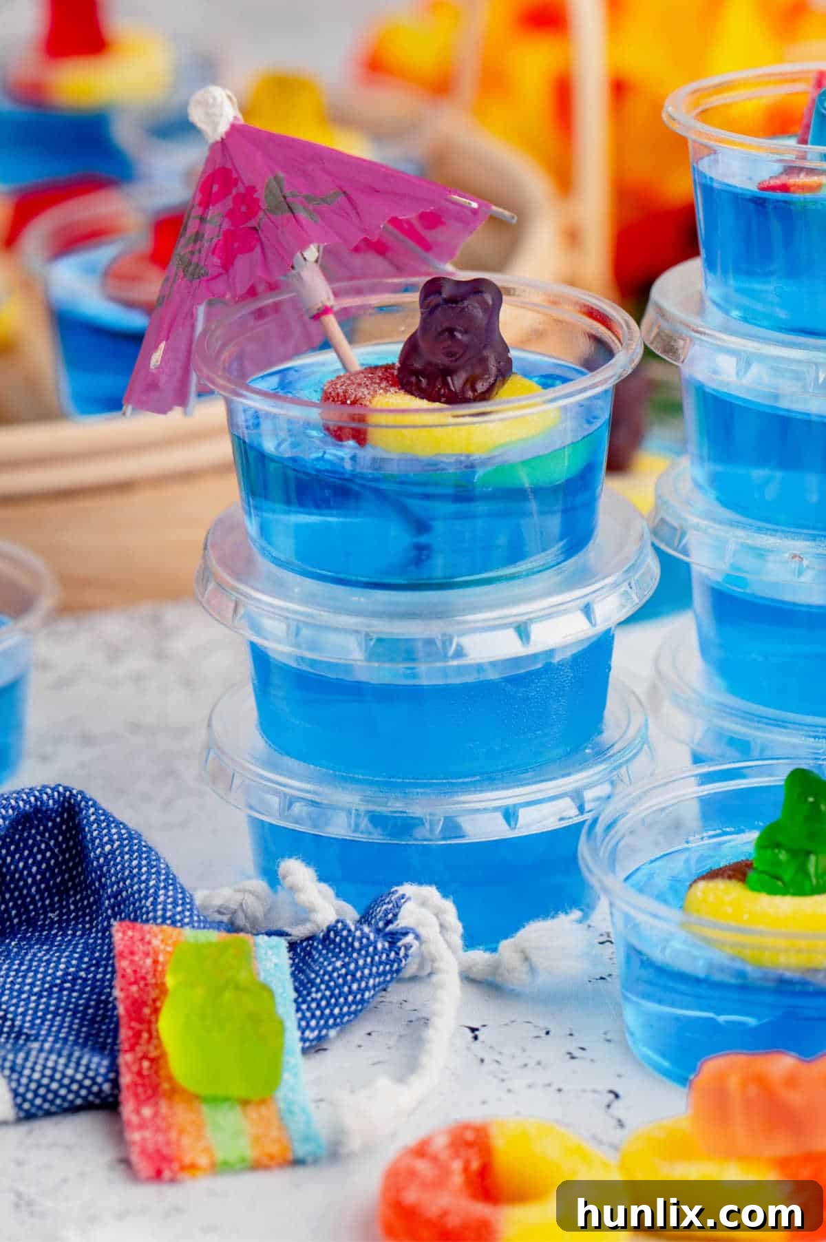 A stack of individual Pool Party Jello Shots in plastic cups, showing the clear blue jello and gummy bear decoration.
