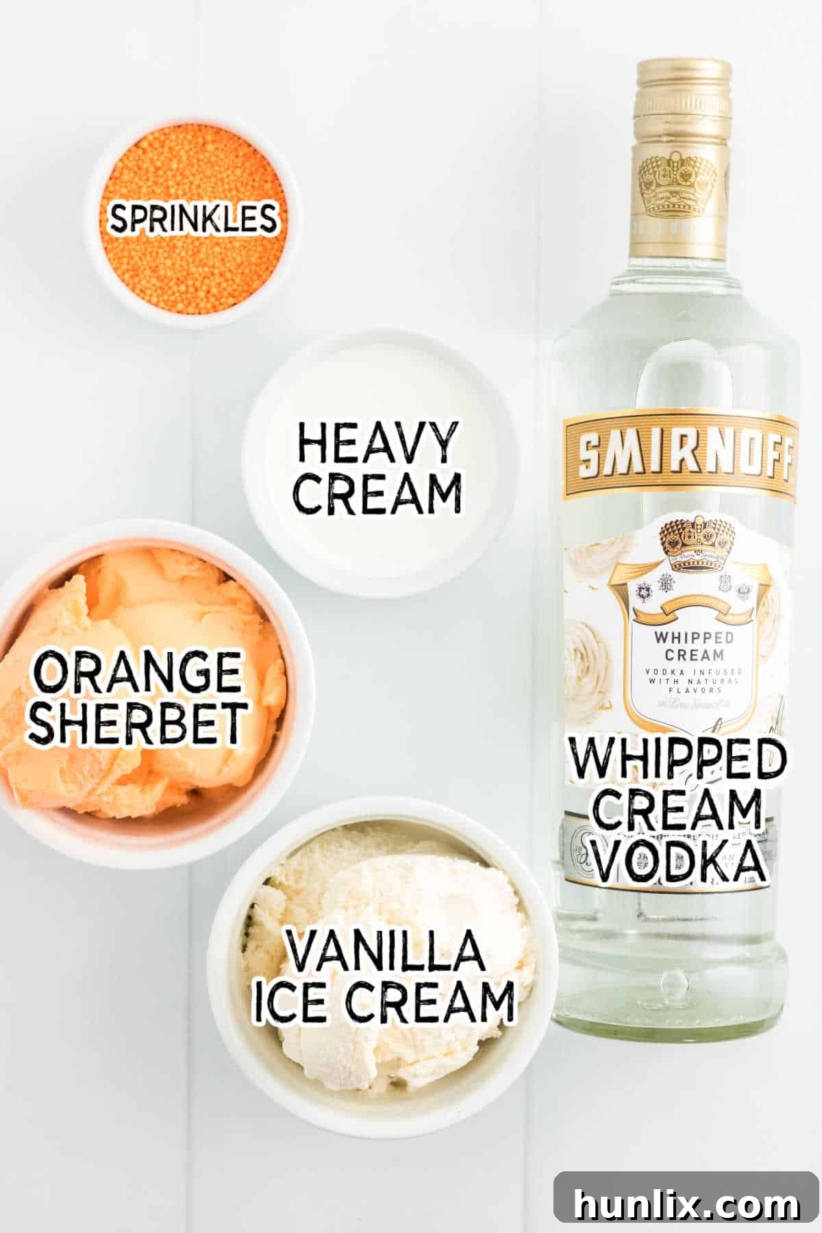 A flat lay of the ingredients for boozy orange creamsicle milkshakes, including vanilla ice cream, orange sherbet, heavy cream, whipped cream vodka, and whipped cream for garnish, arranged on a white background.