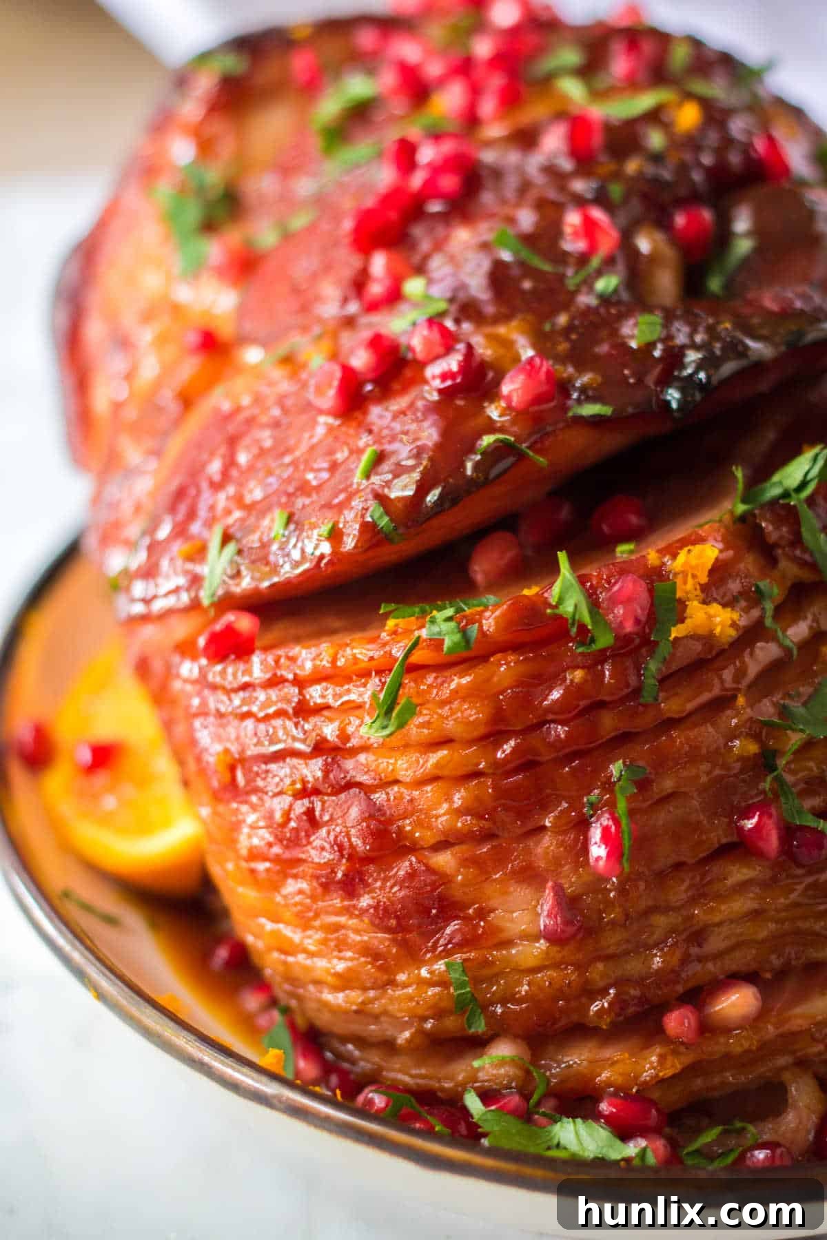 Christmas Glazed Ham 2 A perfectly cooked Christmas ham, glazed with orange and garnished with fresh herbs and pomegranate seeds, on a festive platter.