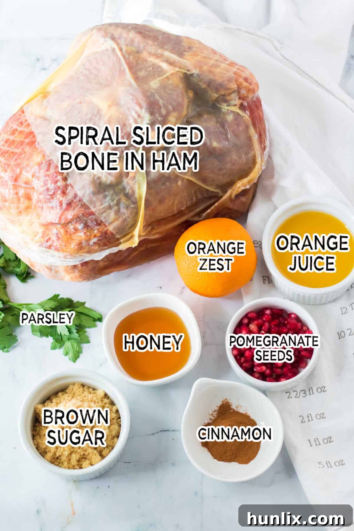 Christmas Glazed Ham 3 Assortment of fresh ingredients laid out for making Christmas ham, including an orange, honey, cinnamon sticks, brown sugar, and pomegranate seeds.