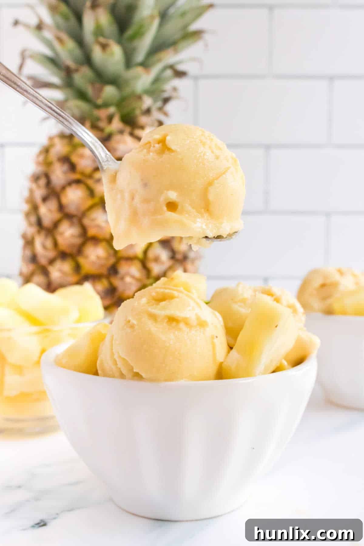 Pineapple ice cream on a spoon over a bowl of ice cream.