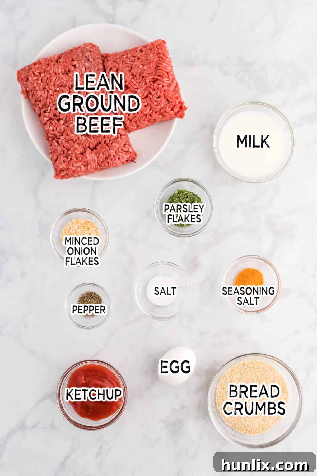 Meatloaf ingredients laid out on a wooden surface, including ground beef, eggs, breadcrumbs, milk, and various seasonings.